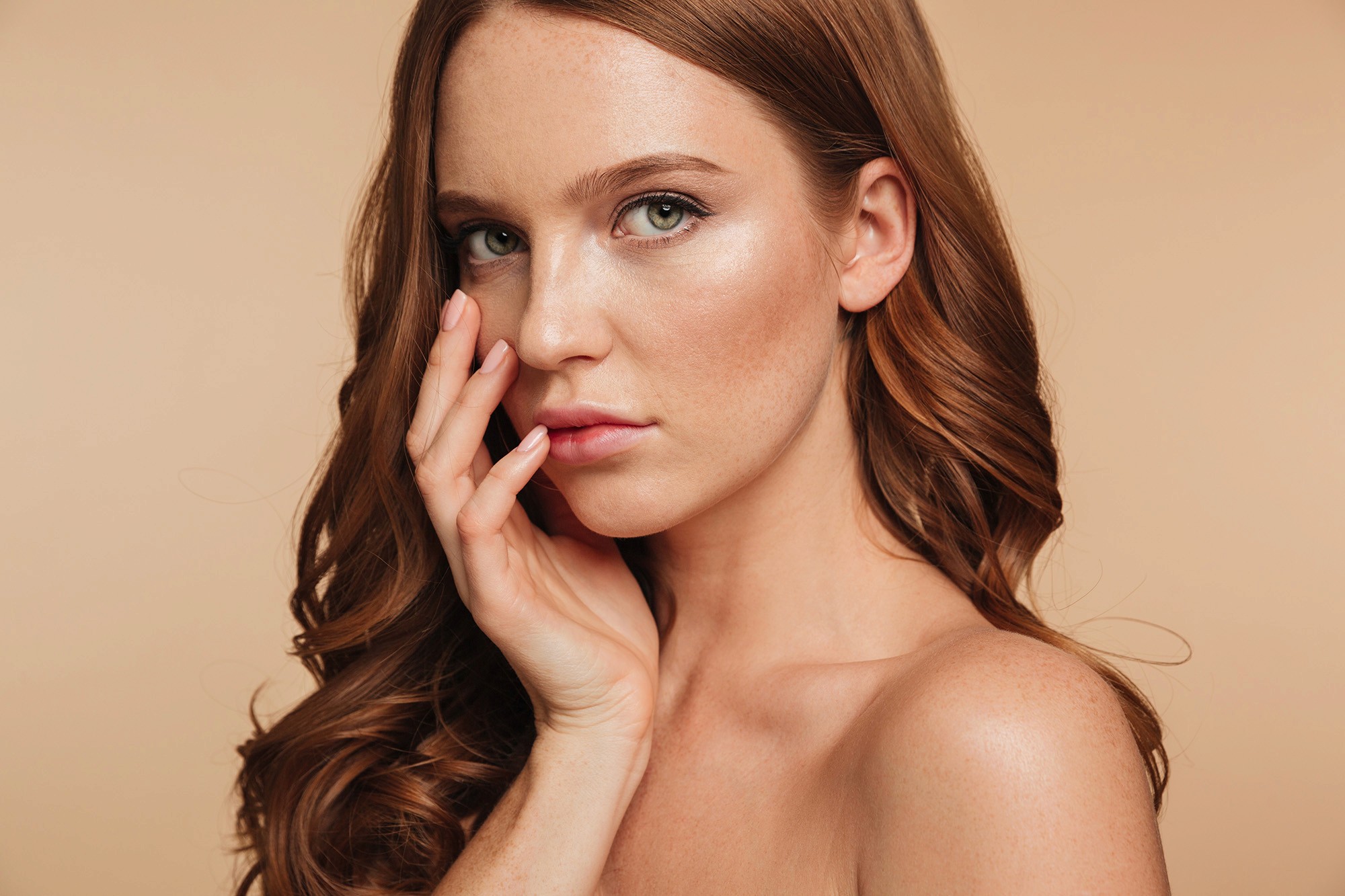 Portrait of a woman with long red hair gently touching her face, looking into the camera