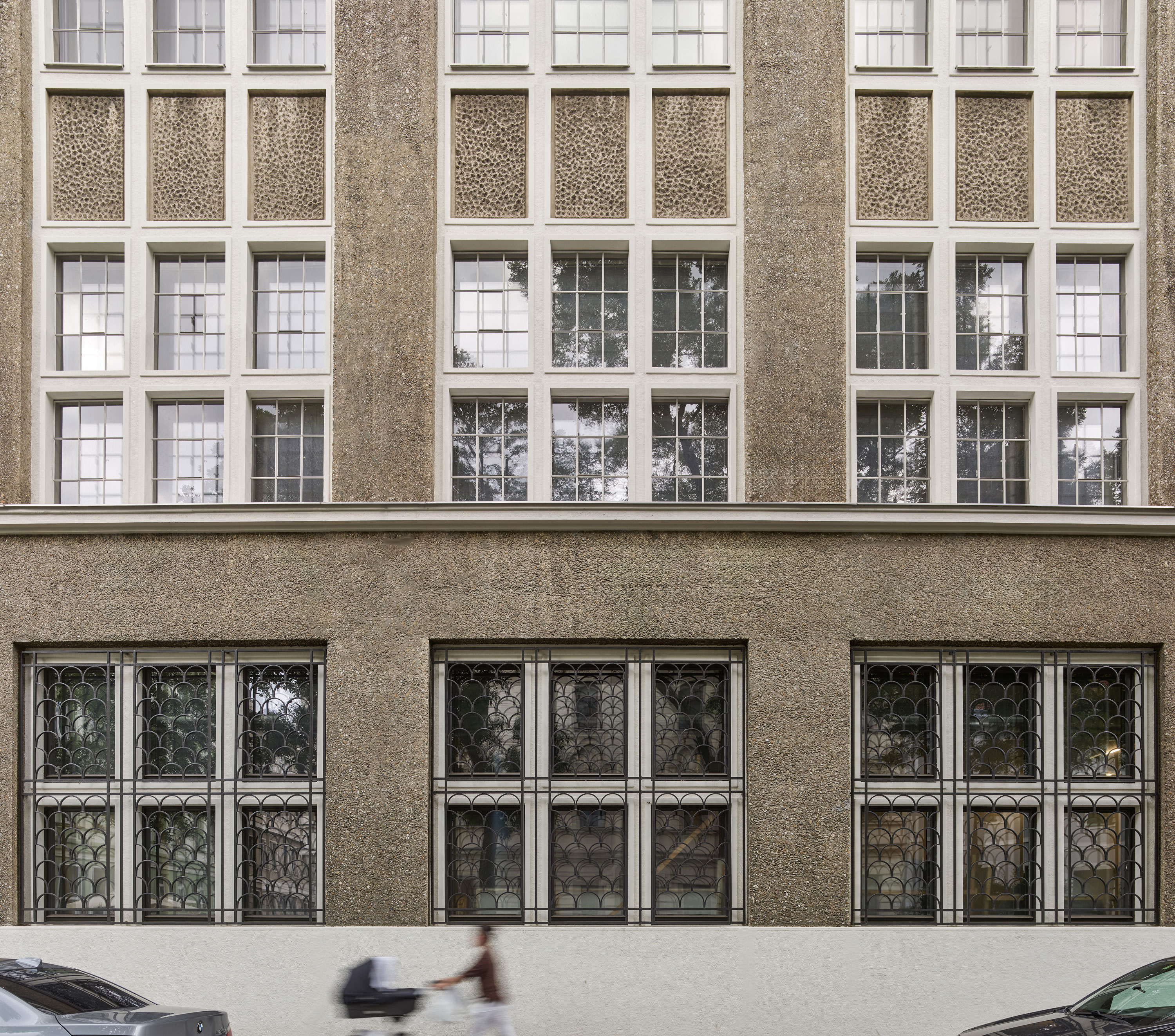 Fassade des Dorotheum Depots mit zwei Fensterreihen, darunter drei große Fenster mit historischen Gittern, davor verschwommen Mensch mit Kinderwagen und parkende Autos.