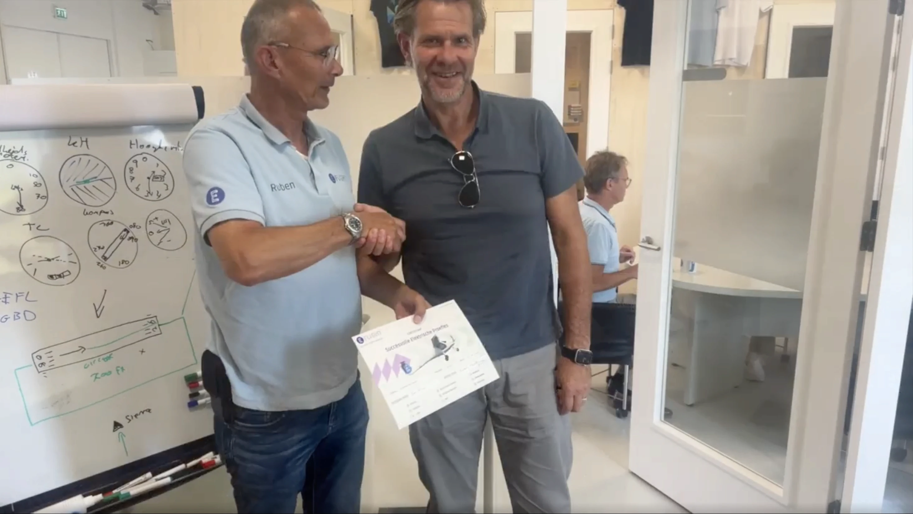 Instructeur feliciteert student met eerste elektrische solovlucht en overhandigt proeflescertificaat.