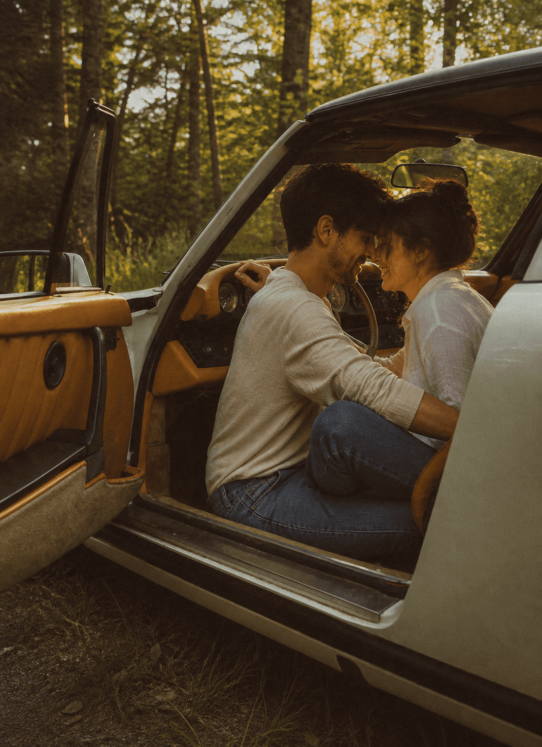 Couple sitting together in the open door of a vintage car in the woods