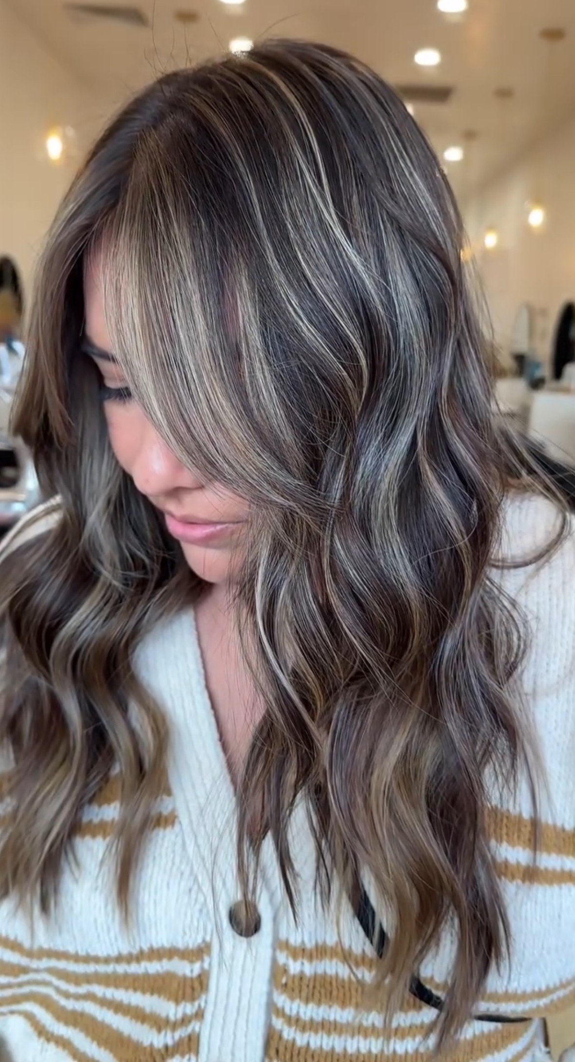 Side view of medium-length brunette hair with cool ash babylights and face-framing layers, styled in soft beachy waves for a natural, blended finish.