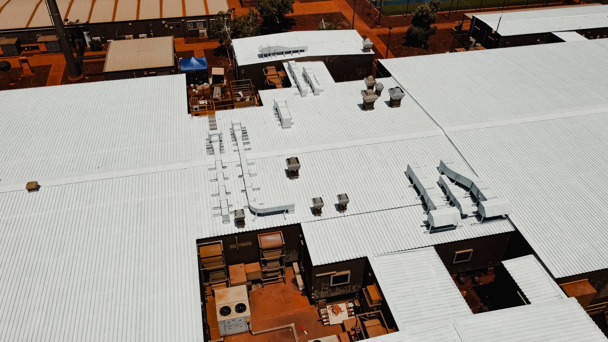 Aerial view of a white metal roof on a large industrial building with HVAC vents and ductwork, located in remote Australia.