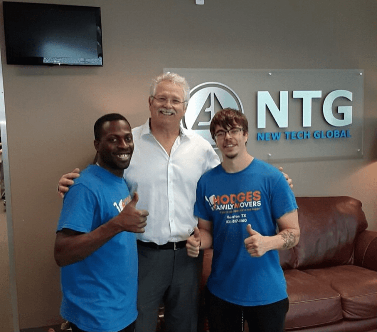 Smiling commercial client standing between Hodges Family Movers commercial movers in Houston office of New Tech Global for post-move picture