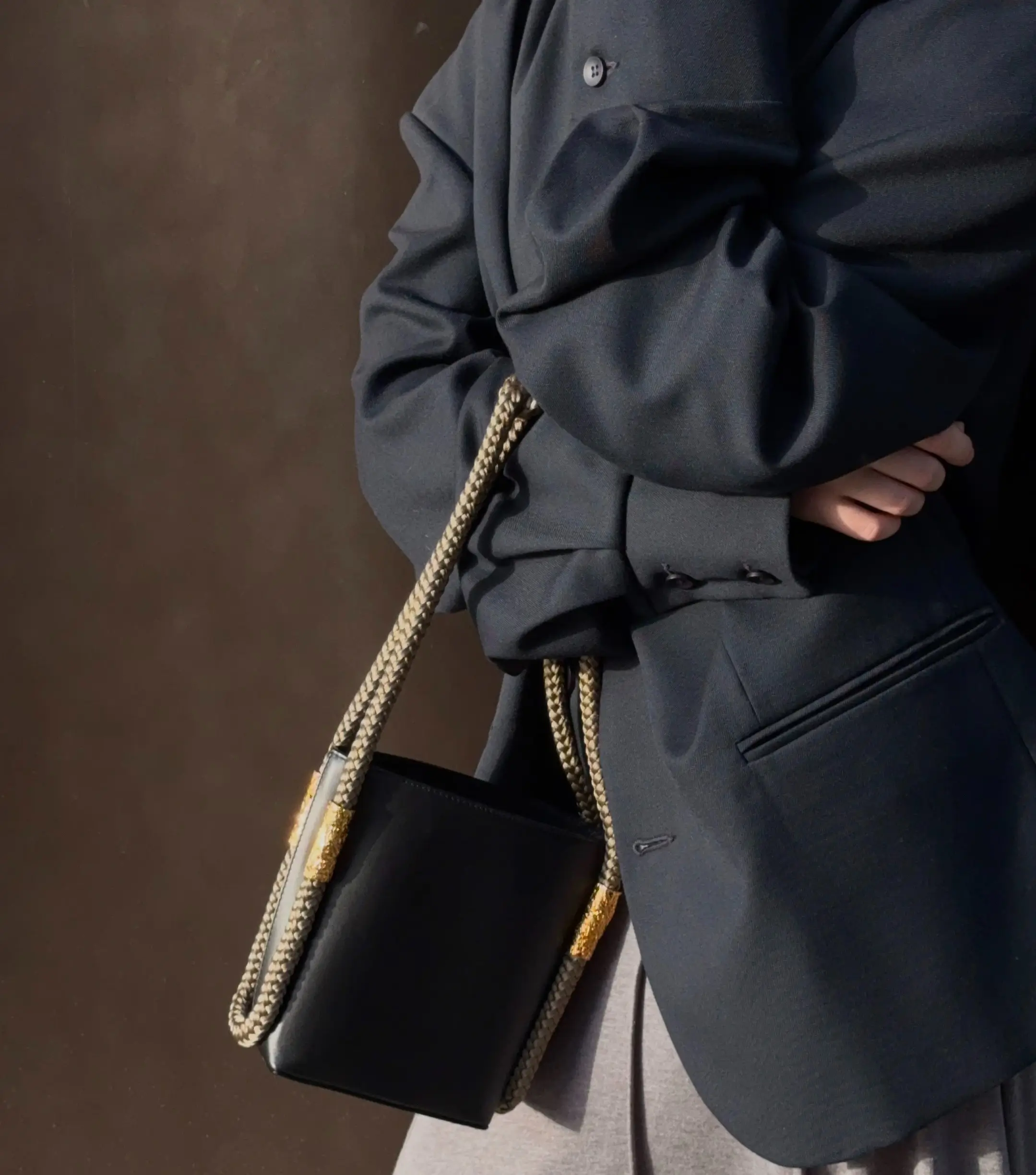 Brown sculptural leather handbag resting on tall ornamental grass during golden hour, evoking a natural, elegant mood.