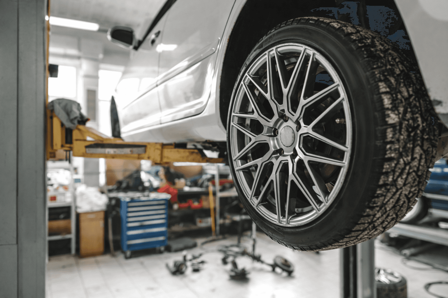 White car lifted in an auto repair shop with a close-up of the wheel and tire.