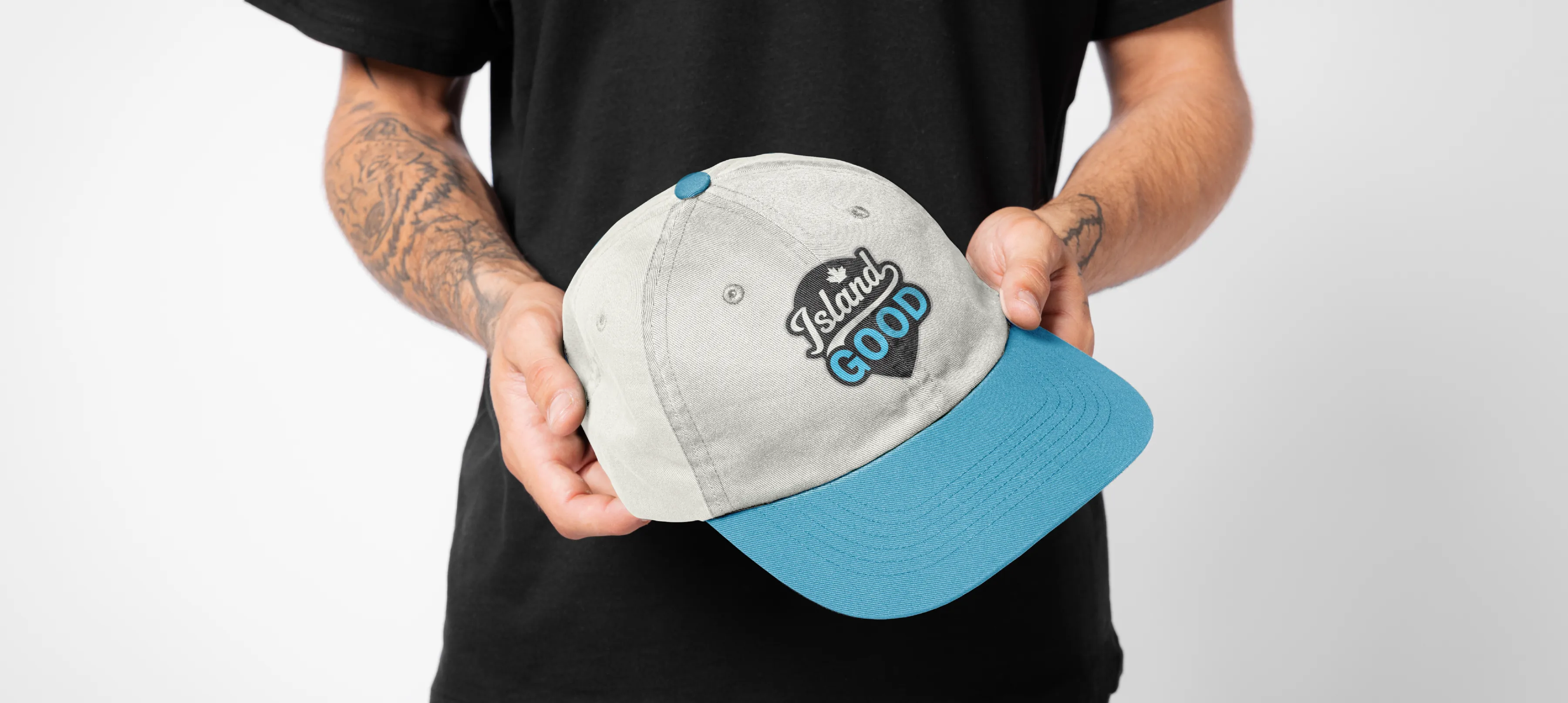 A cream hat with a sky blue button and sky blue brim. On the front of the hat is the Island Good logo.