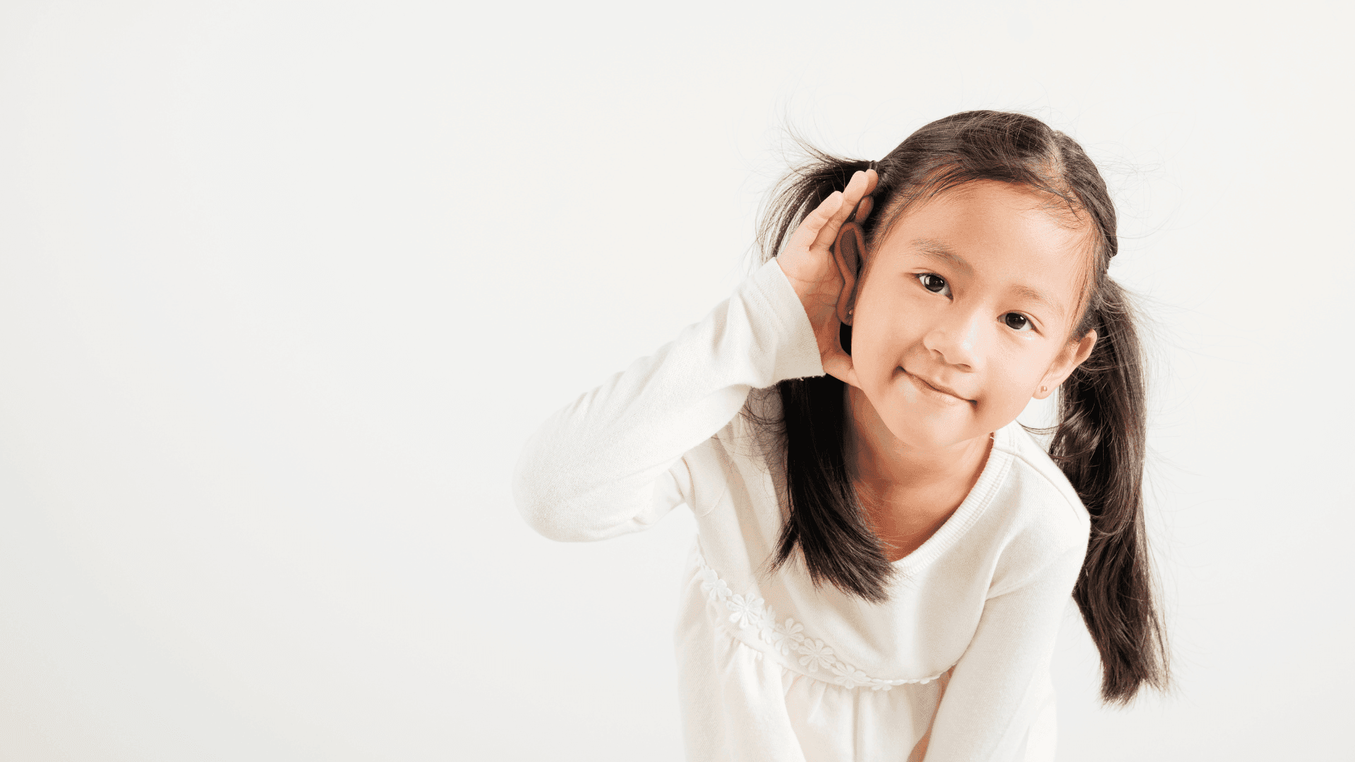A young girl cupping one ear and smiling at the camera.