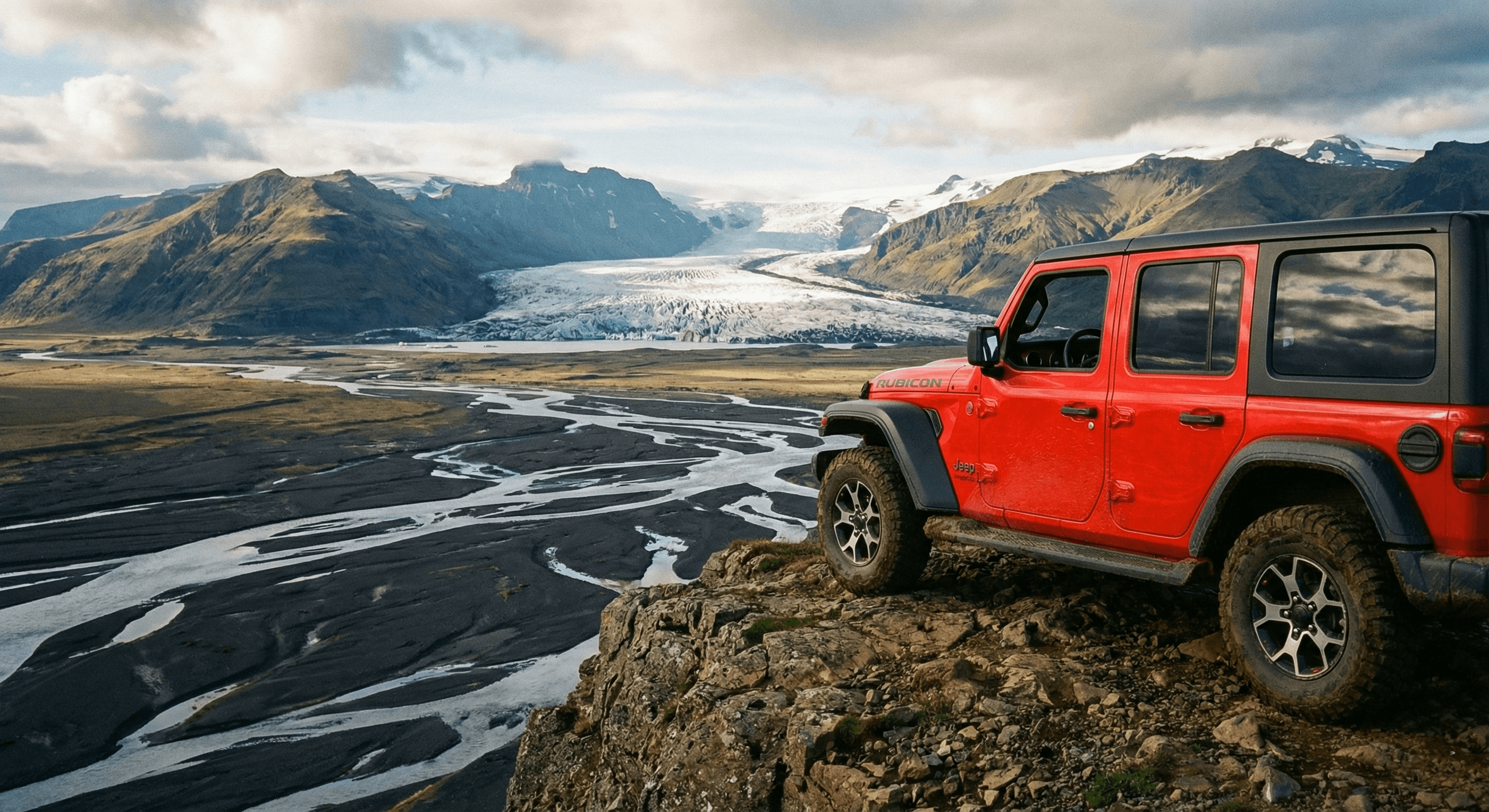 A red Jeep Wrangler parked on a rocky cliff edge overlooking a vast river valley.