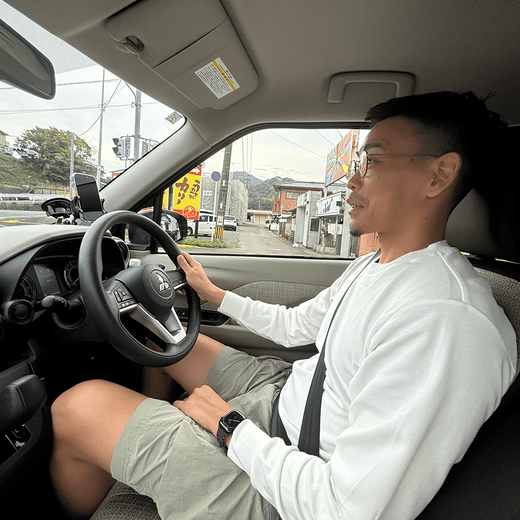A side view of a male in a shirt shirt inside a car with his right hand on the steering wheel