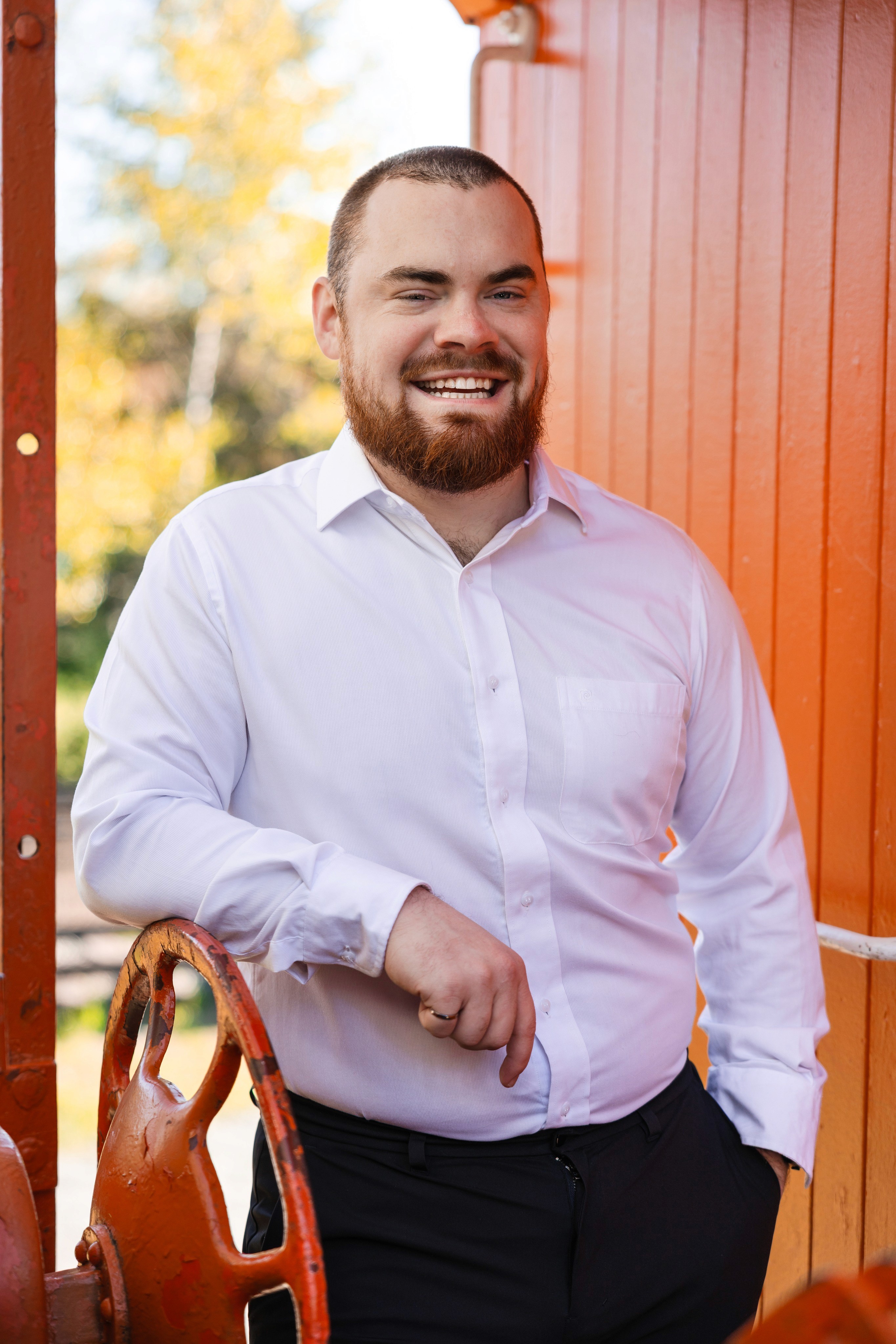 Jake in a white shirt leaning on the brake wheel of an orange caboose