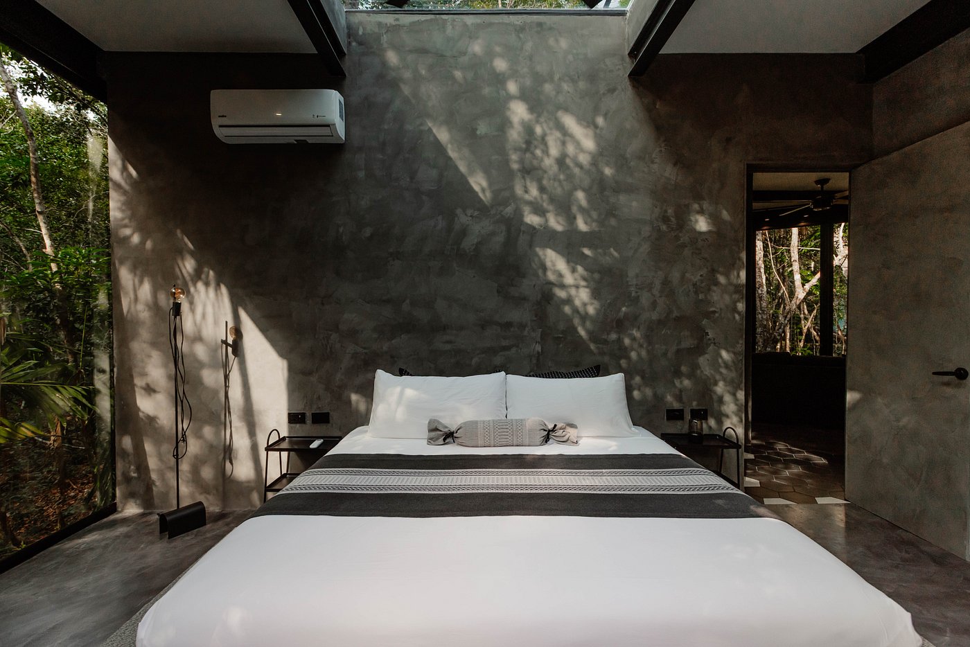 Three people are carefully removing a fresh loaf of artisanal bread from a rustic, wood-fired brick oven, with flames visible inside.