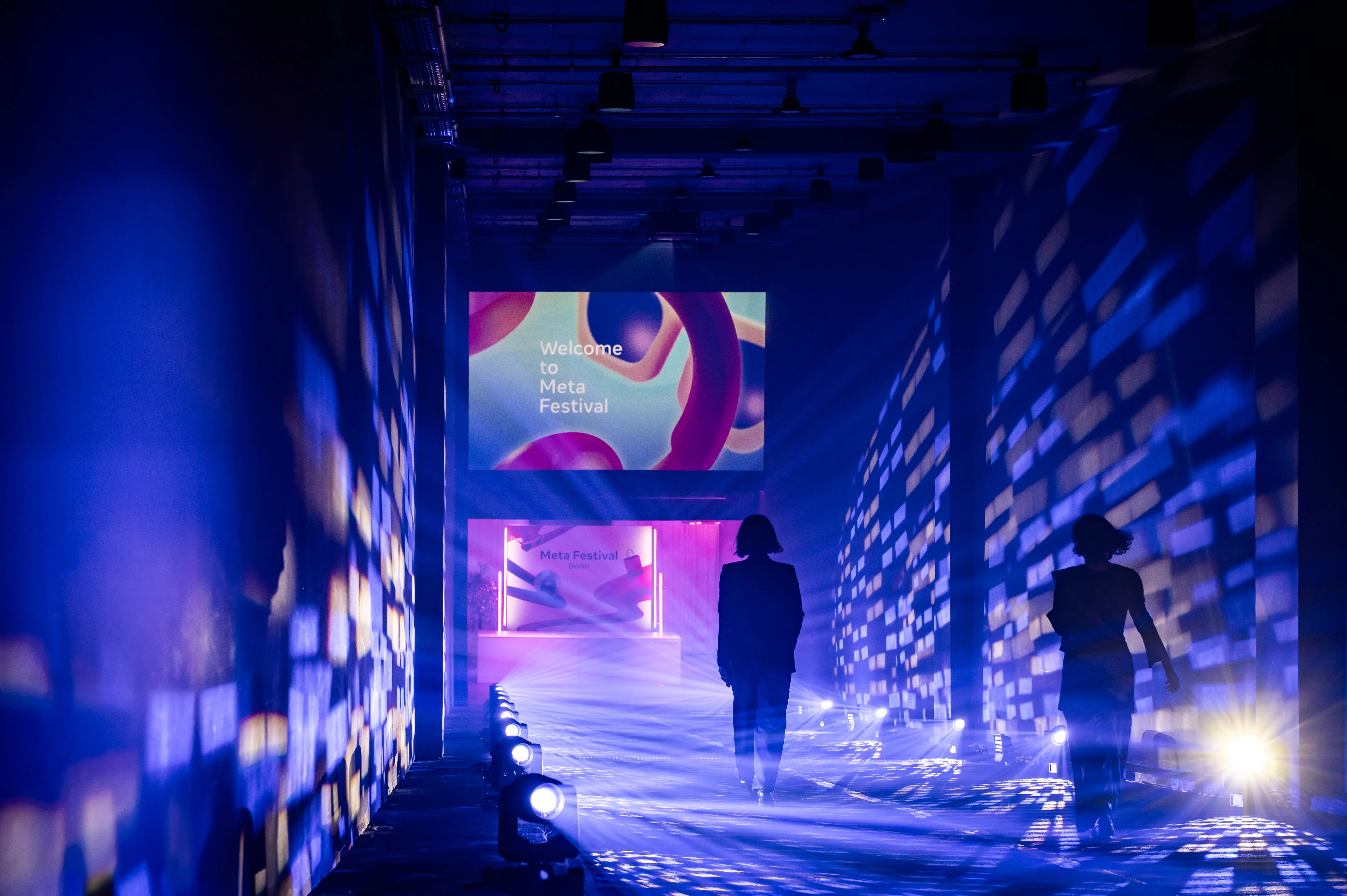 Guests walking through the blue-lit corridor with light pattern walls toward the festival screen.
