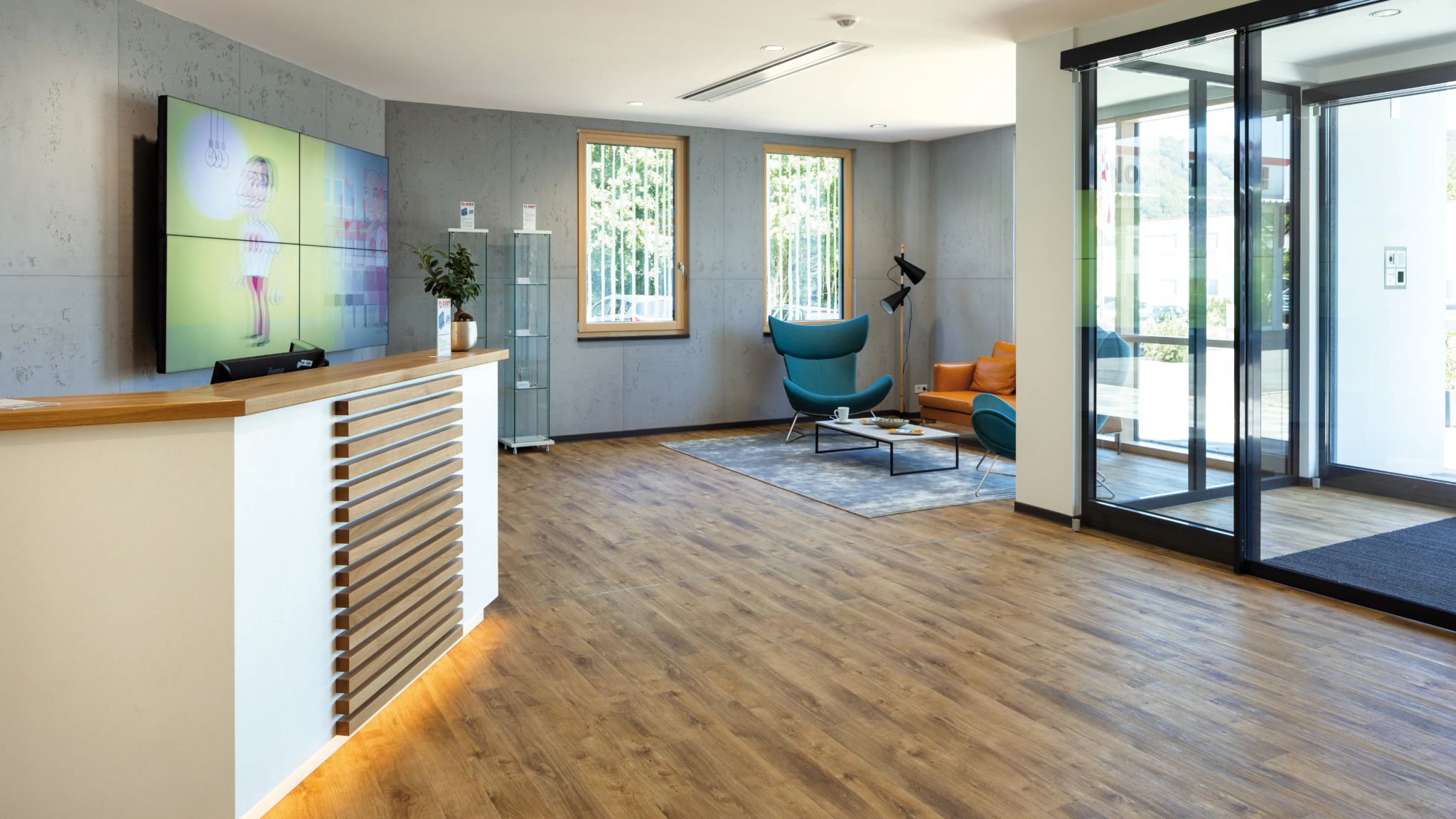 Empfangsbereich in einem Bürogebäude mit Theke, Sitzecke und einer Glastür.