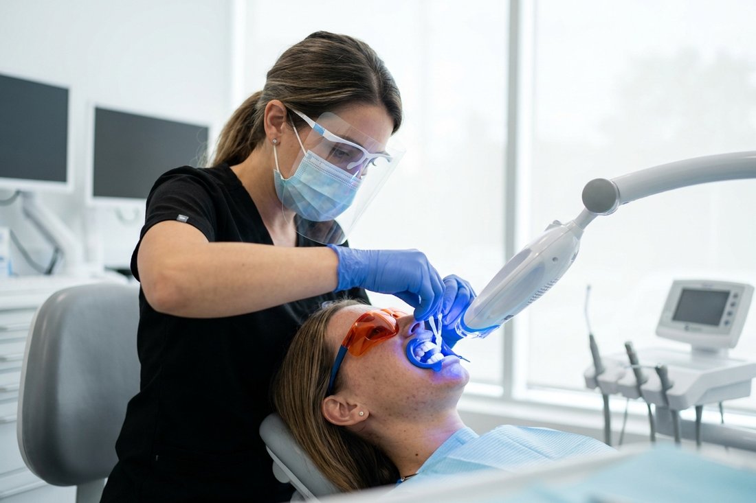 Dentist performing an in-office teeth whitening treatment with a blue LED light