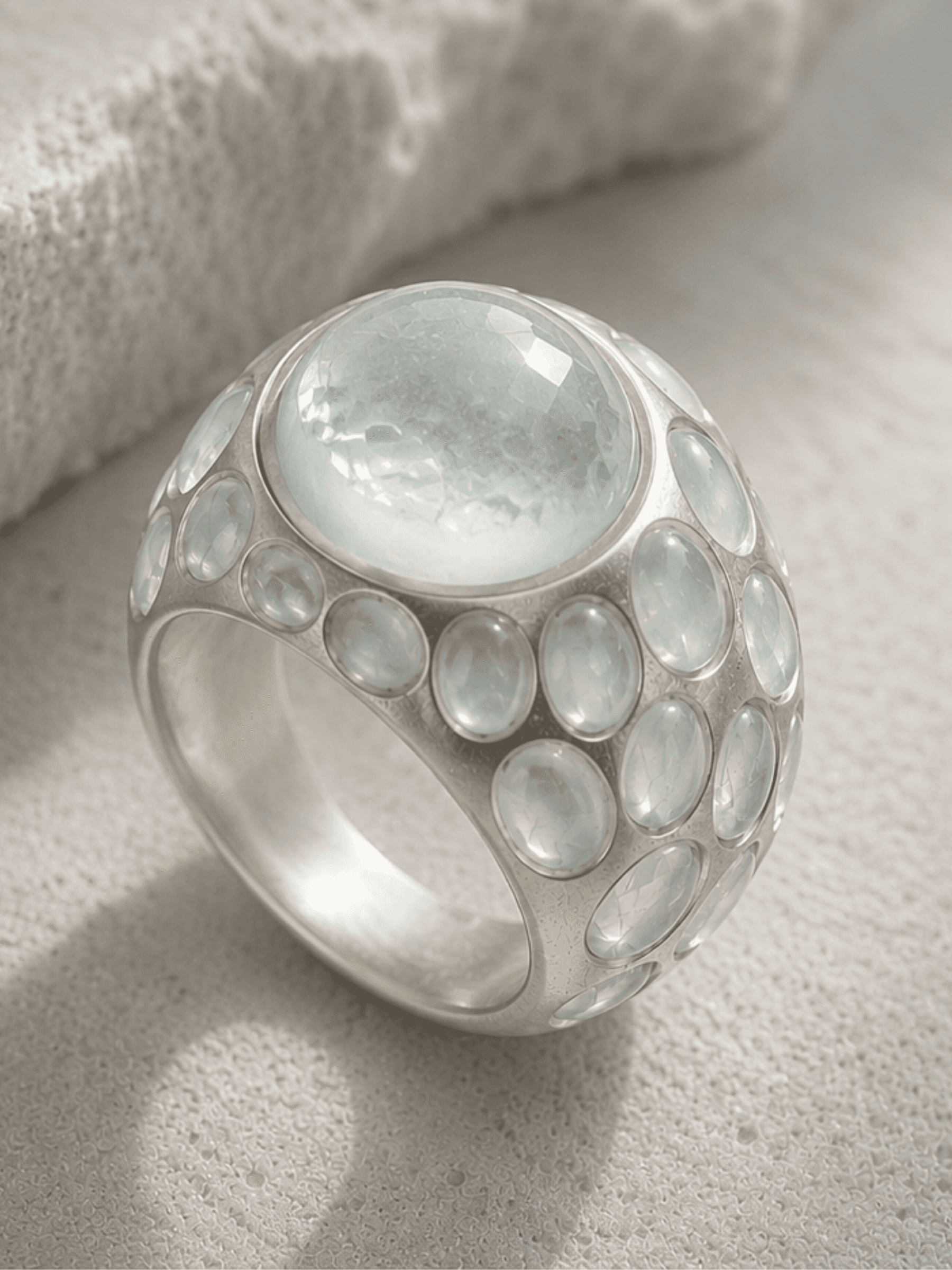 Sculpted Light ring in brushed sterling silver featuring a pale aquamarine centerpiece surrounded by smaller aquamarines on a textured mineral surface.
