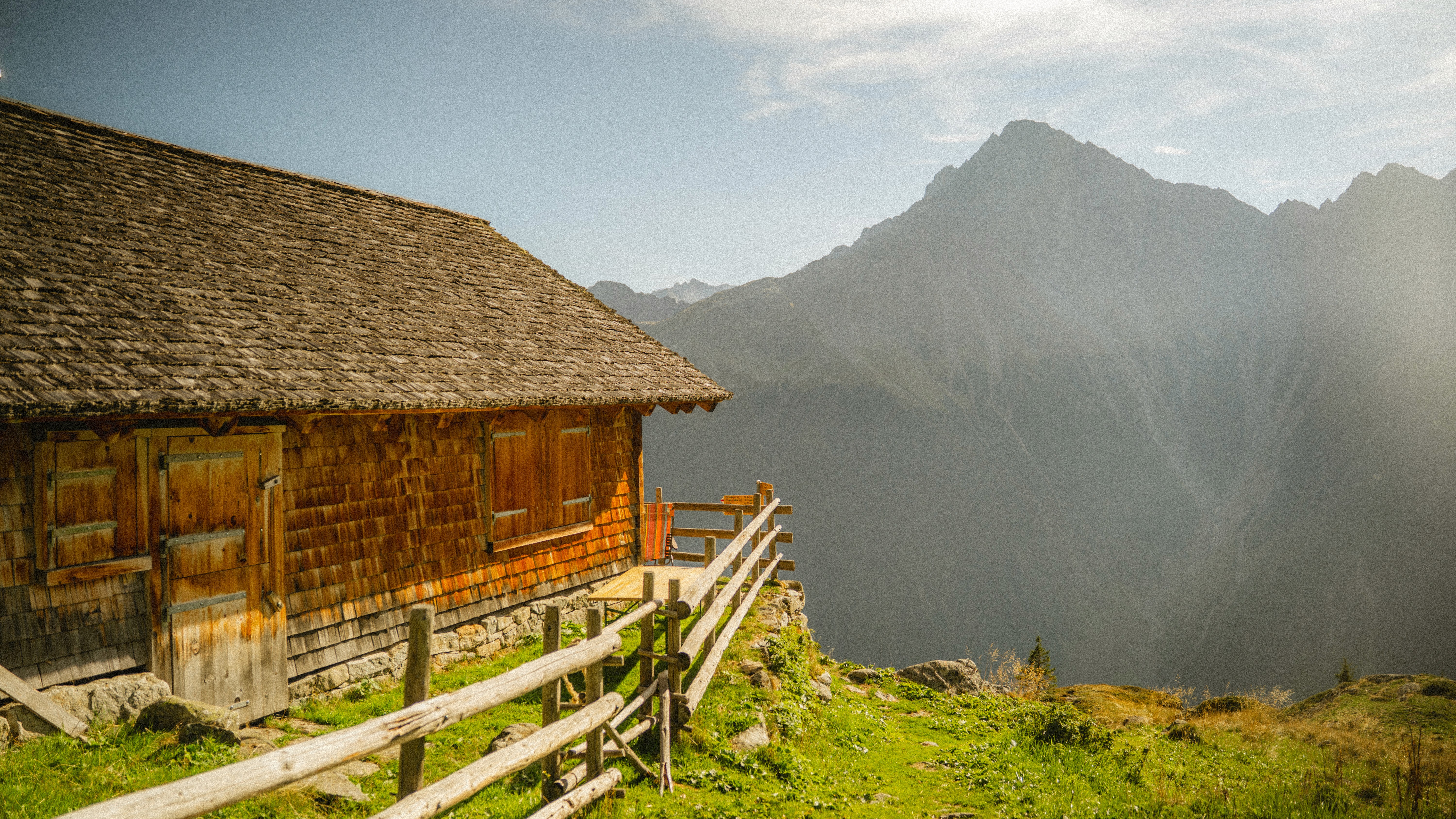 Verwitterte Alphütte mit Holzzaun vor dunstigen Berggipfeln