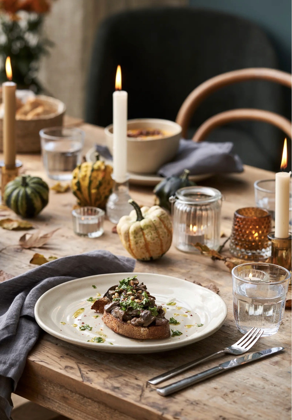 Assiette en grès blanc-beige avec tartine aux champignons, sur table en bois décorée de courges, bougies et feuilles d'automne