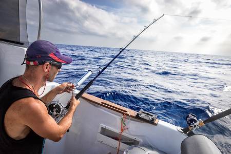 Man in a cap deep-sea fishing from a boat on the open ocean.