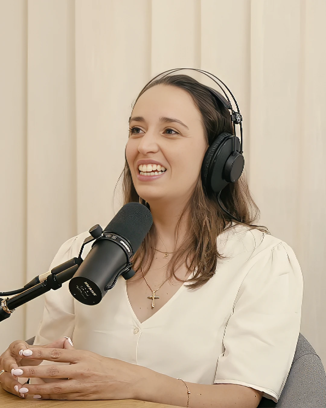 A smiling person with curly hair, wearing a leather jacket, stands in a cozy indoor setting.