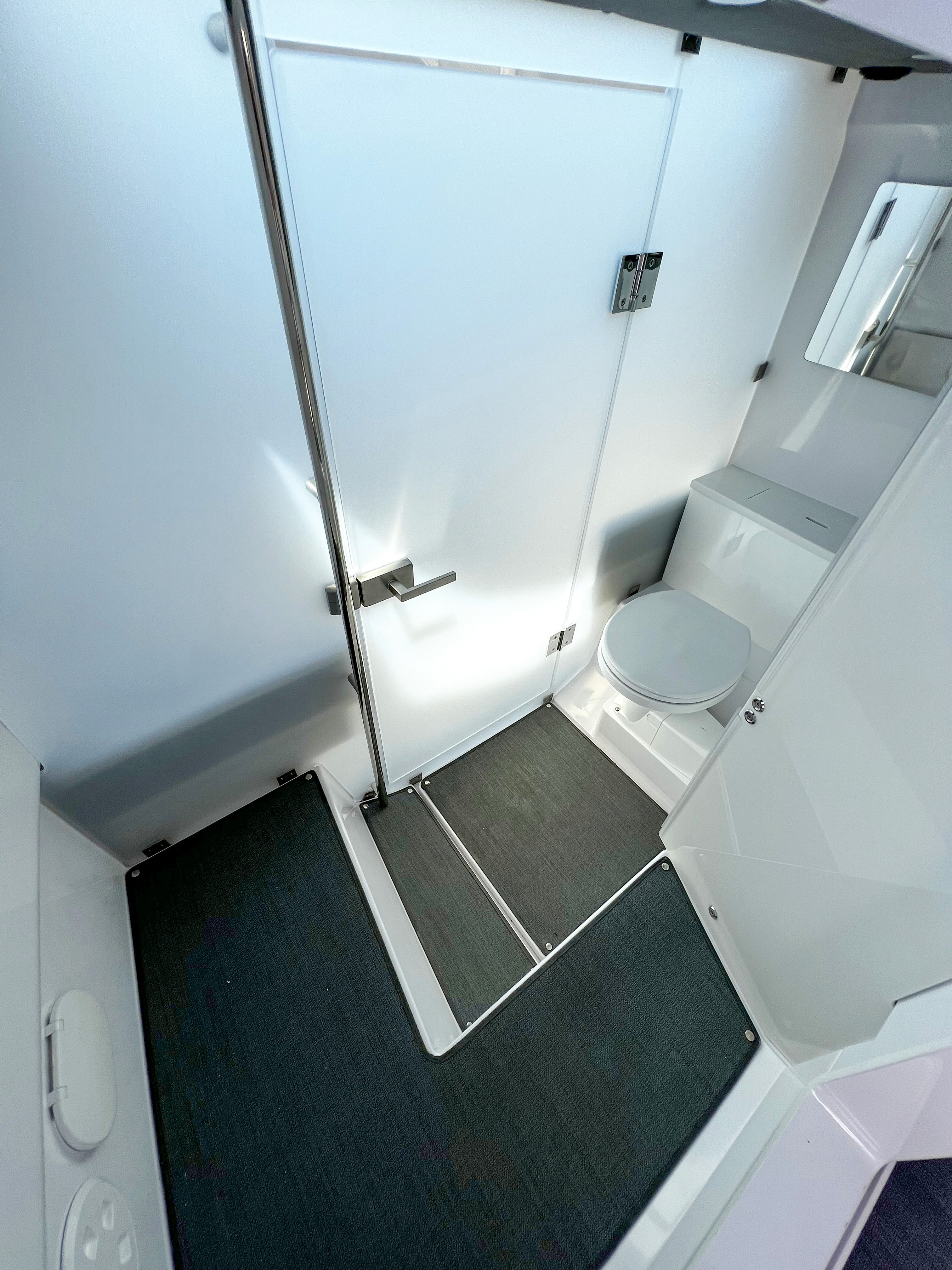 Compact yacht bathroom interior with white fixtures, toilet, sink, and chrome handrail on green carpet flooring.