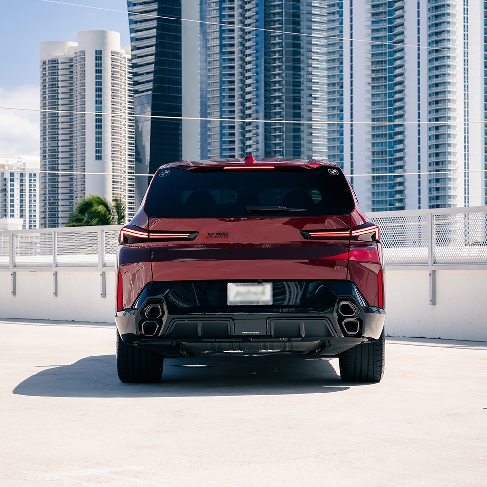 Rear view of a red BMW XM, highlighting its unique stacked quad exhaust pipes and slim LED taillights.