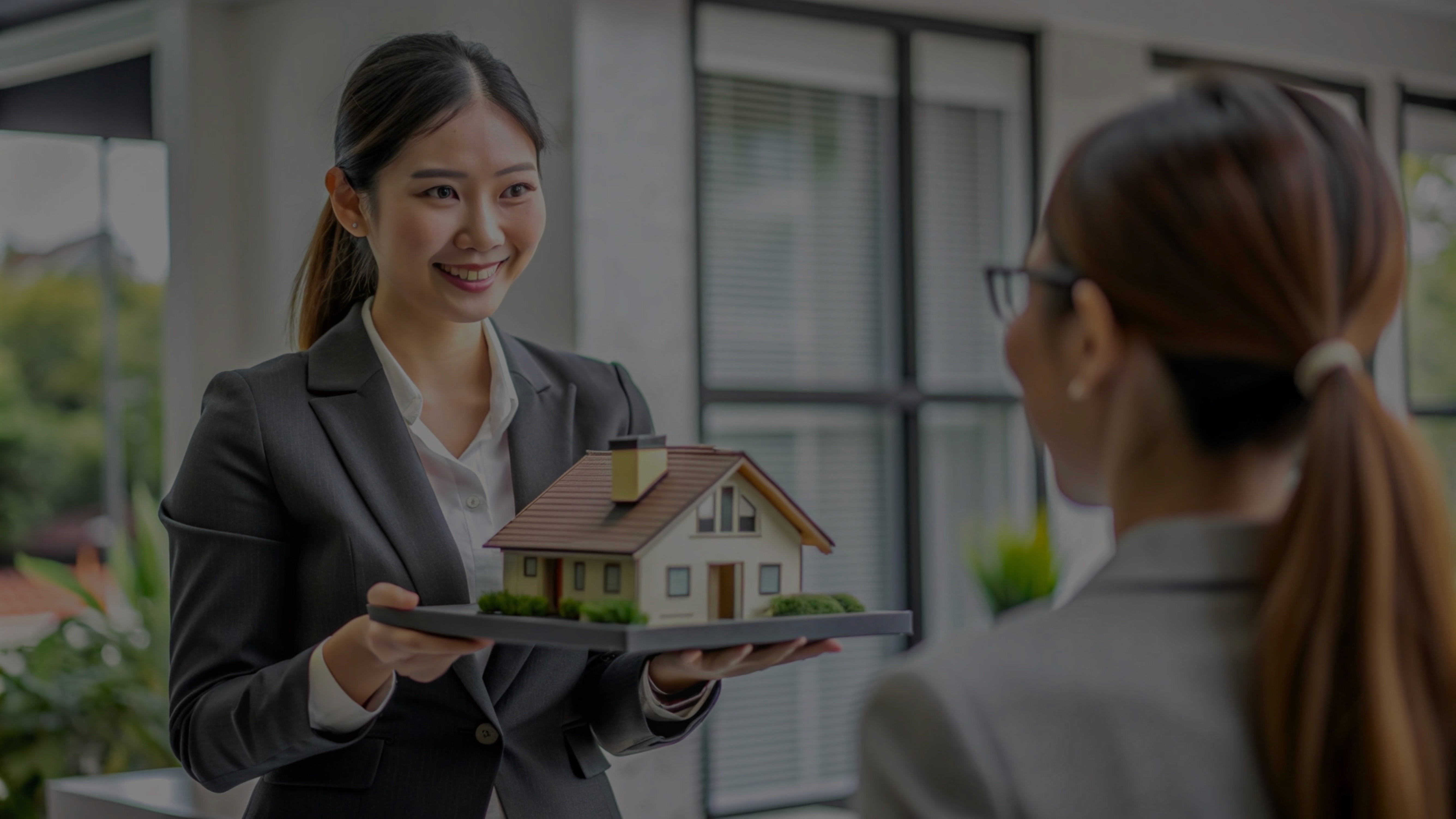 Female real estate agent presenting a miniature model house to a client, symbolizing the sale or handover of a property in Cambodia.