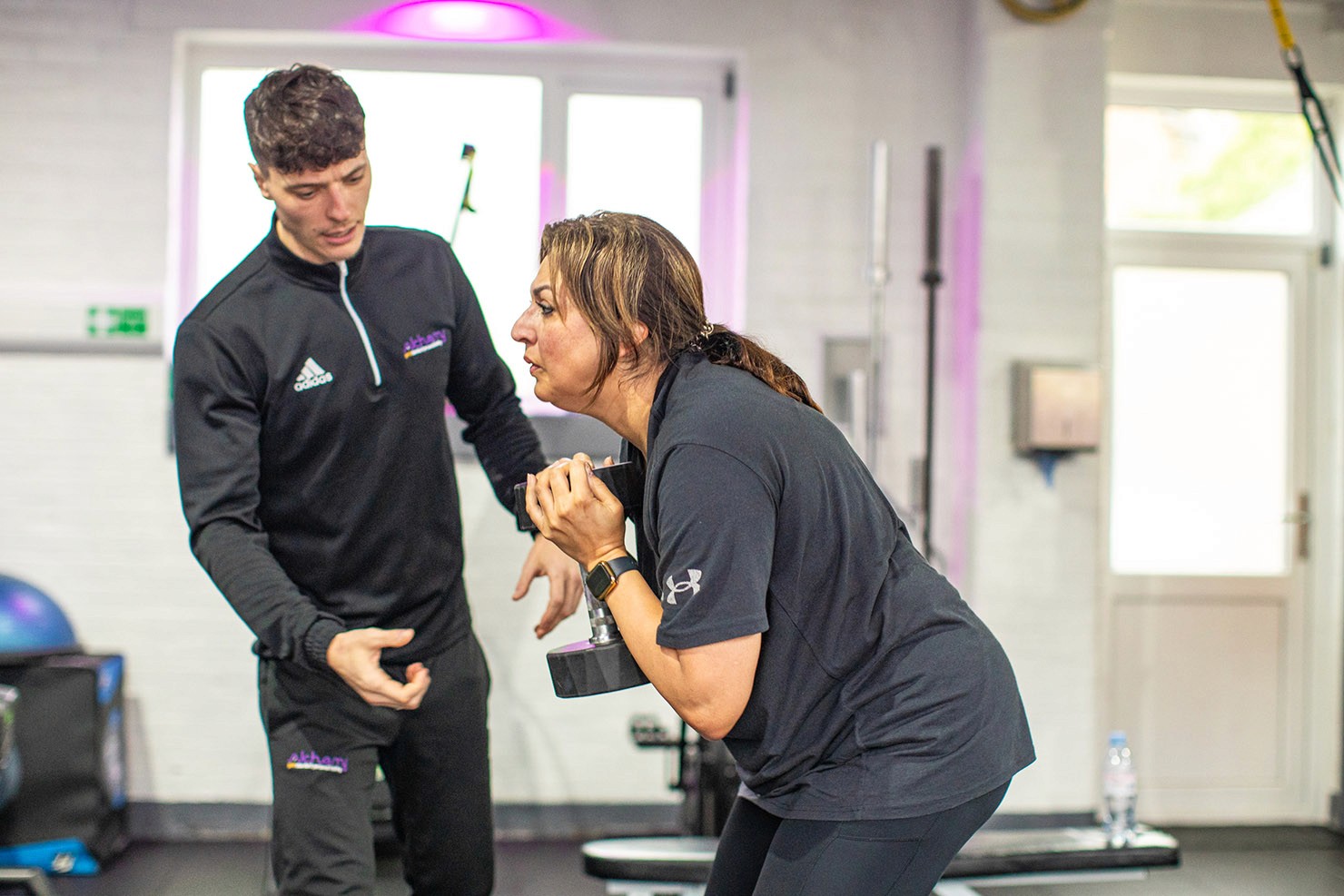 A woman lifting weights with the help of an Alchemy trainer, following a women's fitness plan for beginners