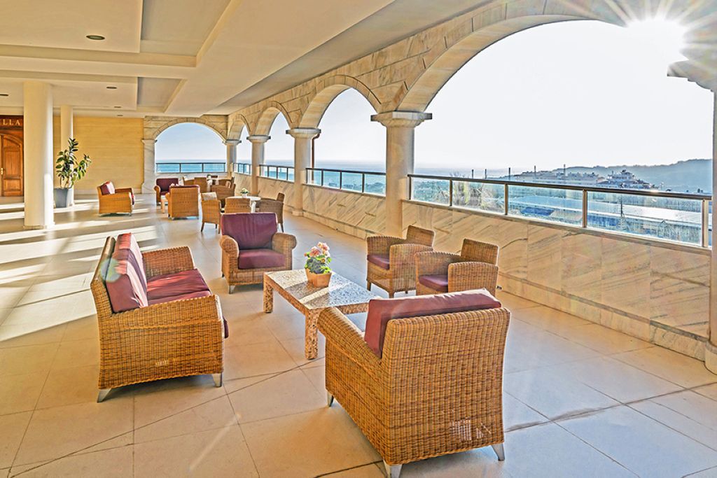 Elegant interior lounge with wooden furnishings, comfortable seating, ocean or sea view through windows, natural lighting, and modern design aesthetic