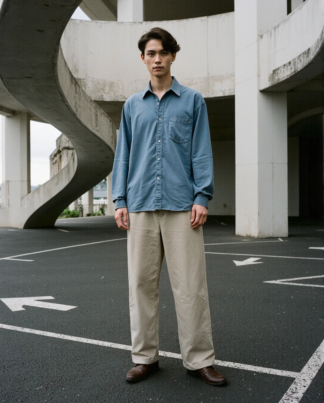 Person in blue button-down shirt and beige pants standing in concrete parking structure with curved architectural elements