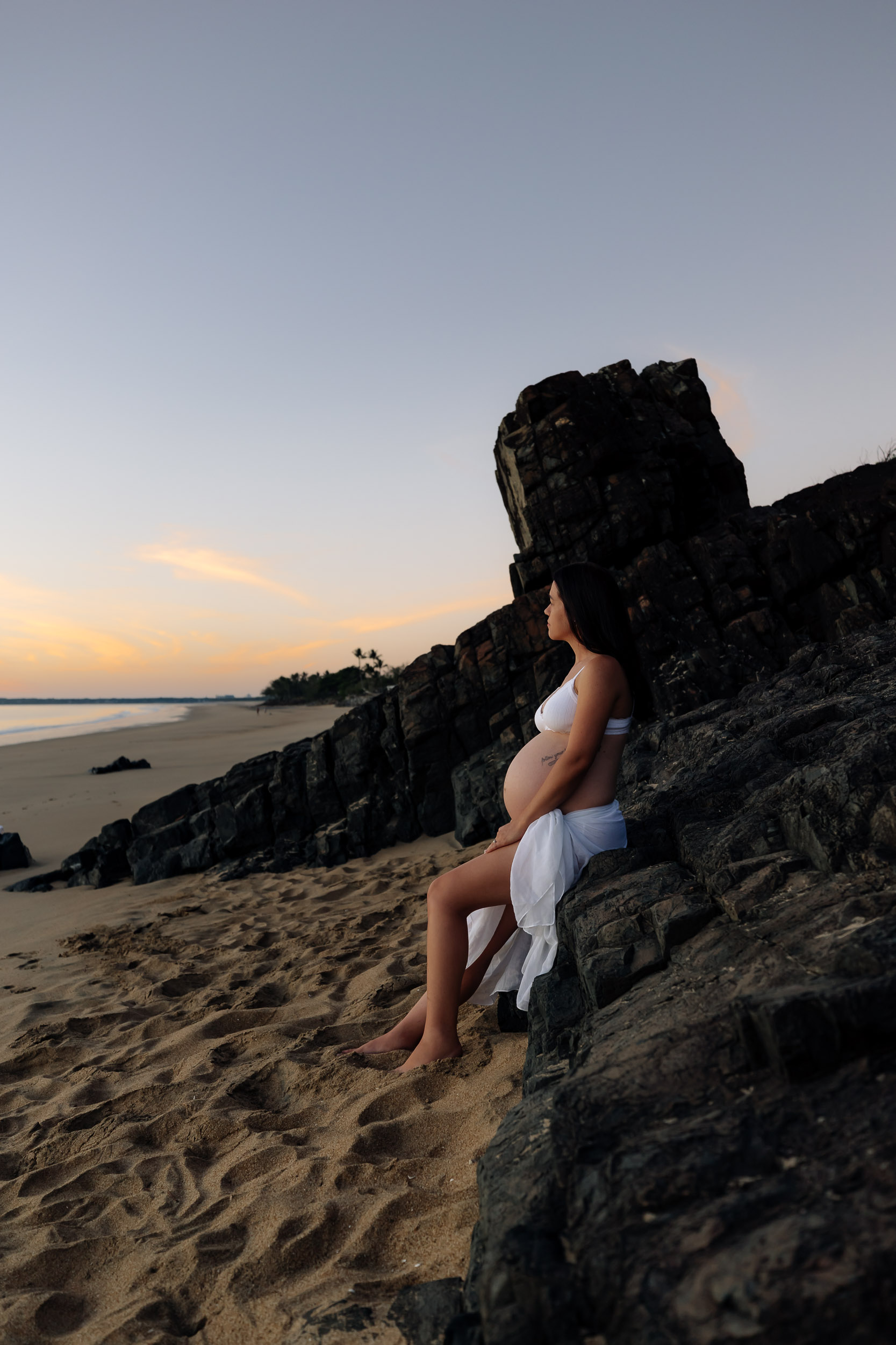 outdoor maternity session Blacks Beach Mackay beach woman in white sitting on rocks at sunrise