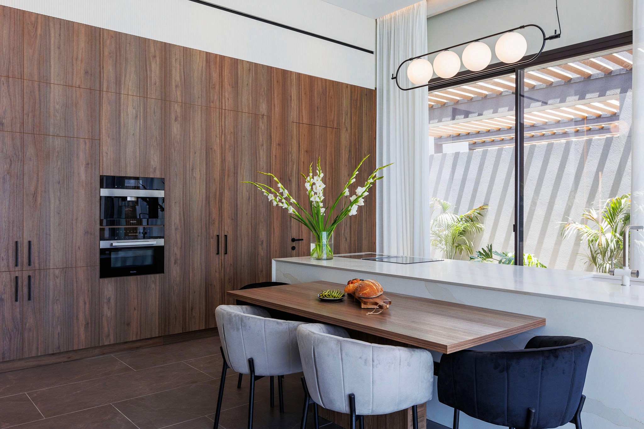 Villa Trio kitchen and dining area with full-height wood cabinetry, island seating, and modern pendant lighting