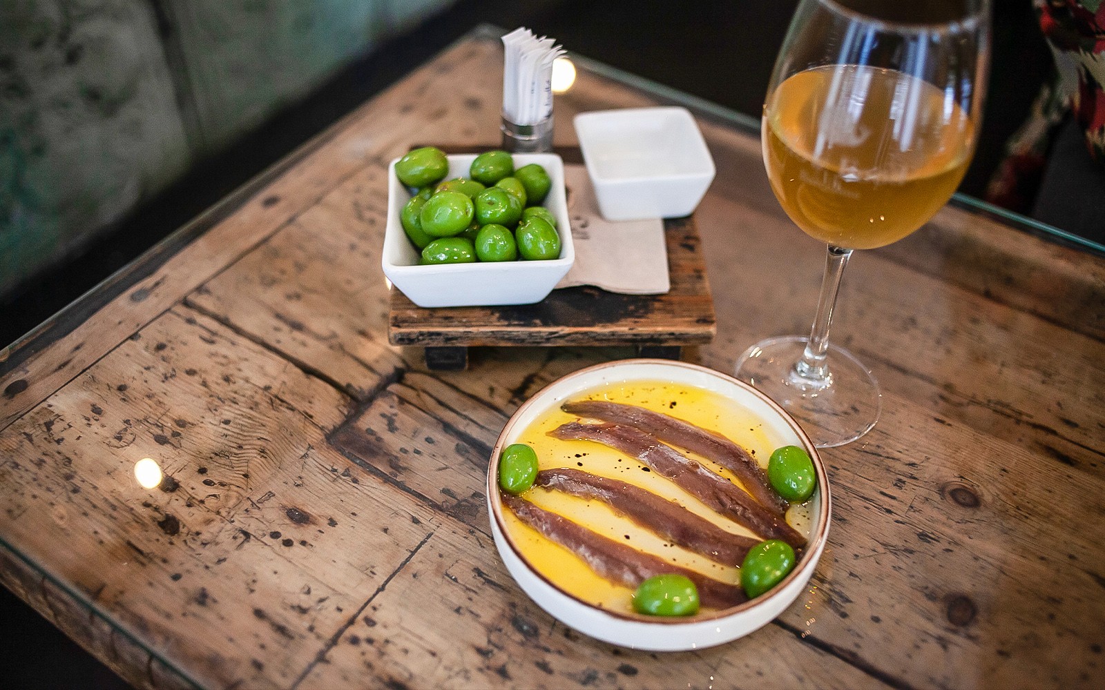 Szardellák és olajbogyók egy tányéron, egy pohár borral, La Barceloneta gasztronómiai túra.