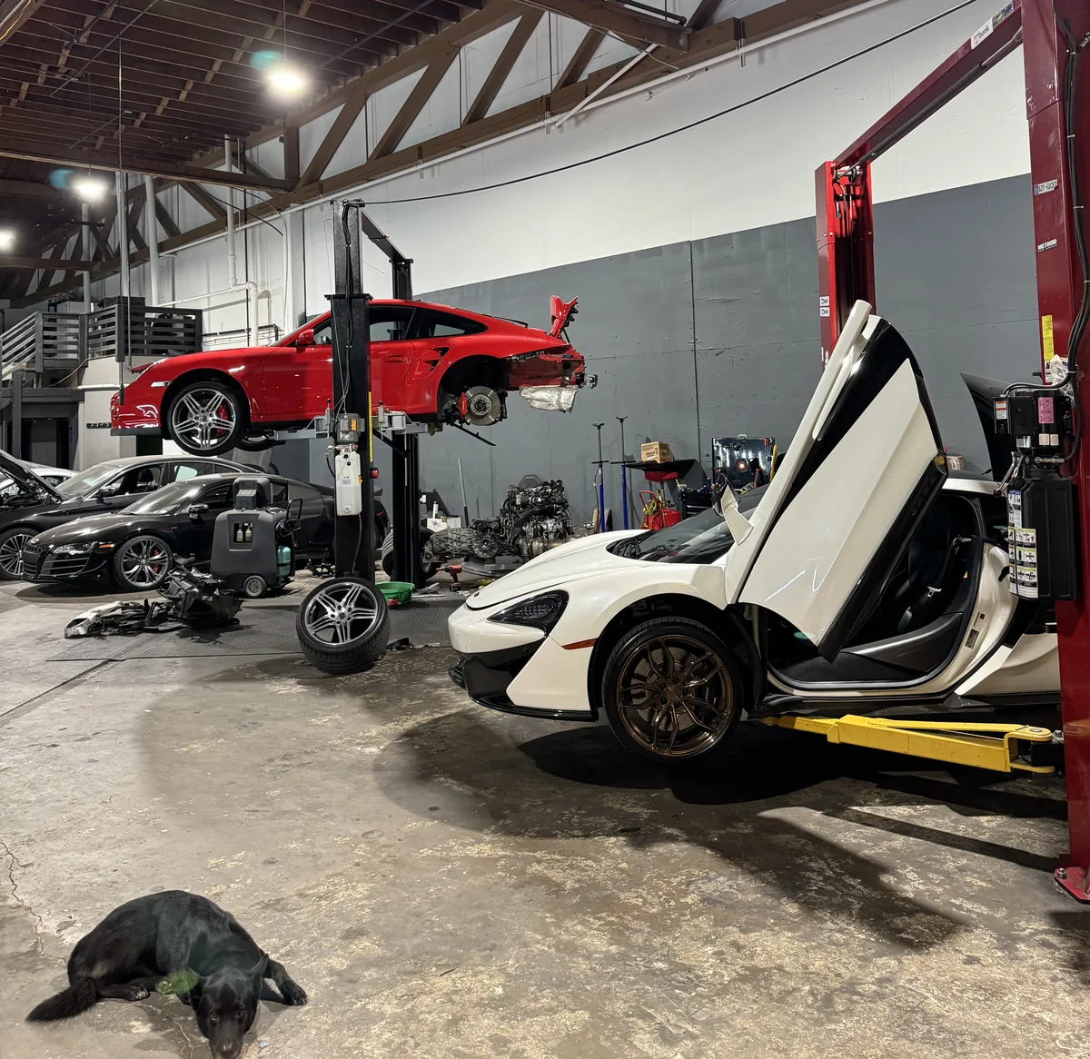 White McLaren with its doors up in the 714 Technik service bay, with a Porsche 911 raised on a lift behind it