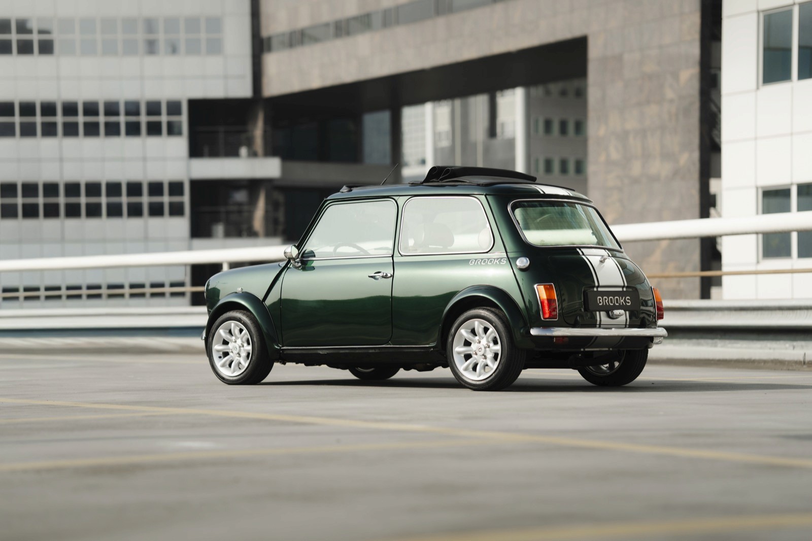 A classic green and white car parked on an open area with modern buildings in the background.