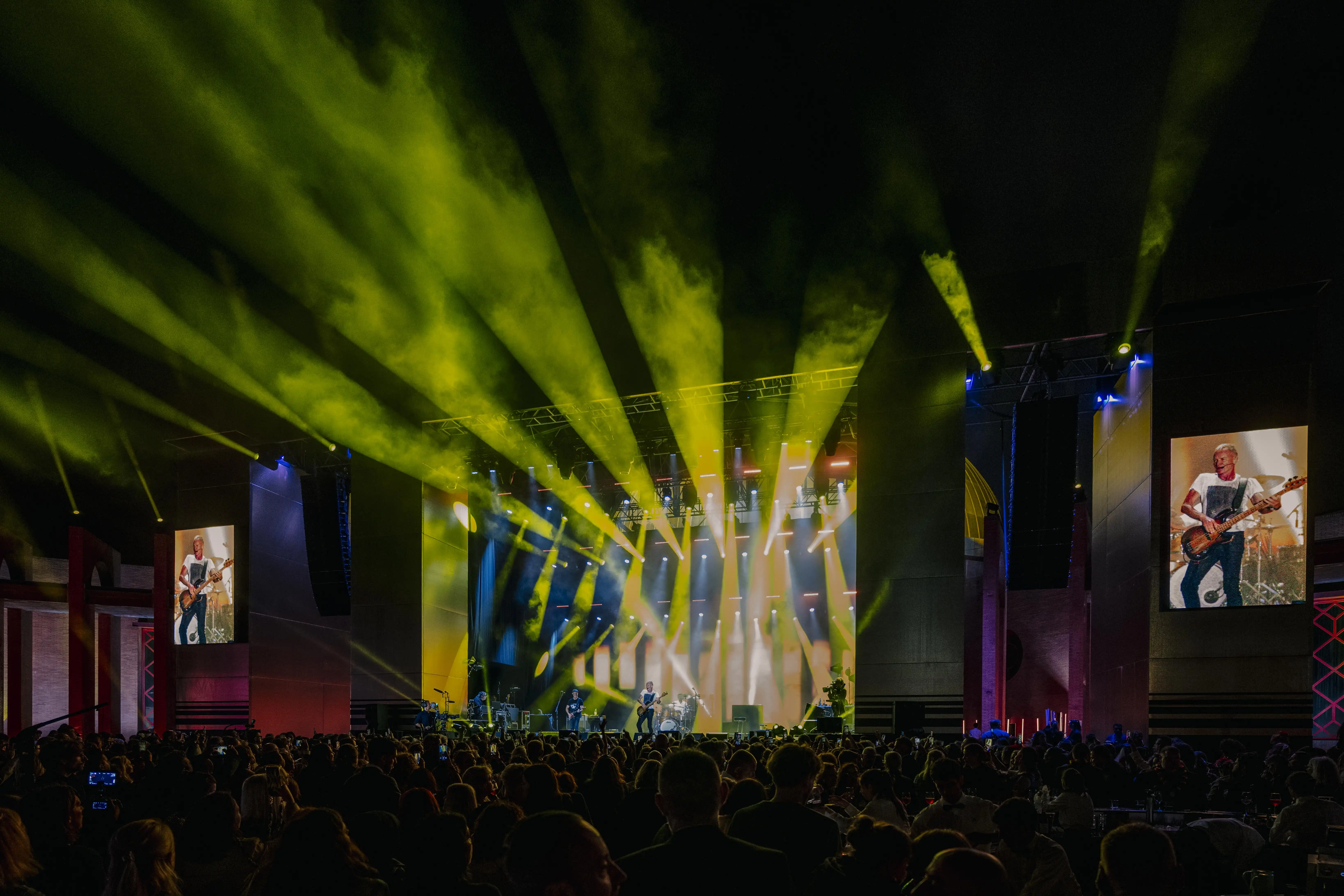 Concert with yellow light beams, band on stage and audience in the arena.