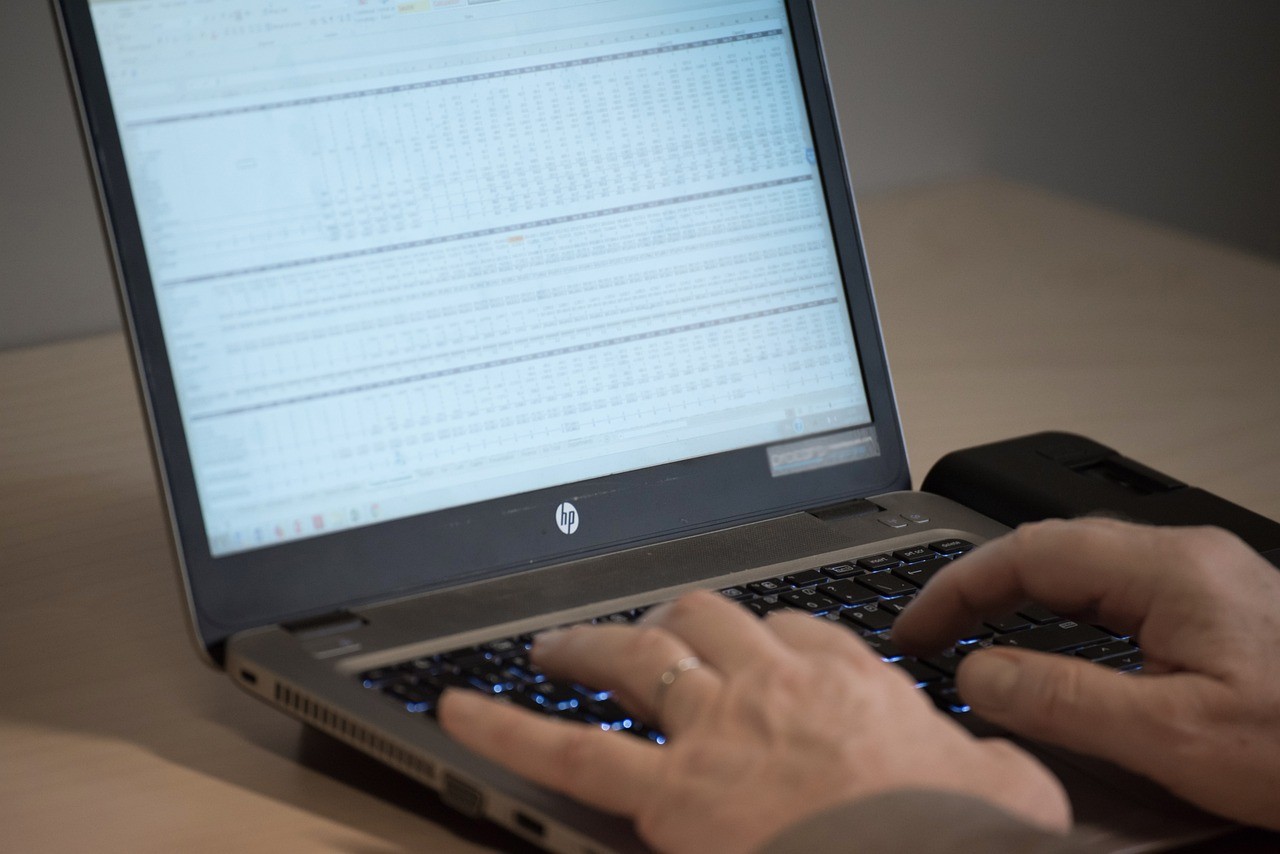 Person typing on a laptop displaying a spreadsheet with rows and columns of financial data.