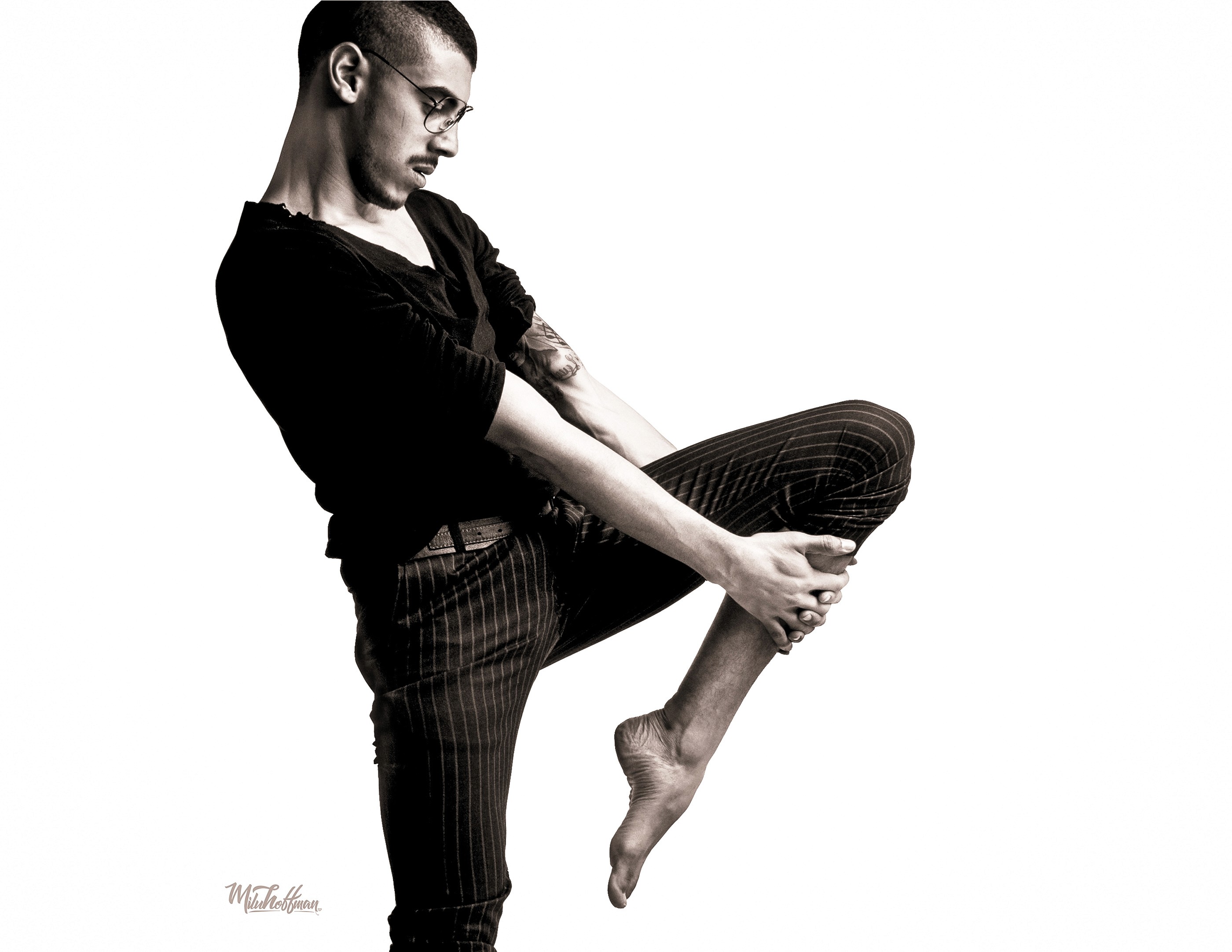 High-contrast black and white studio photography featuring a male subject in a dynamic, sculptural pose, highlighting anatomical geometry and professional-grade chiaroscuro lighting.