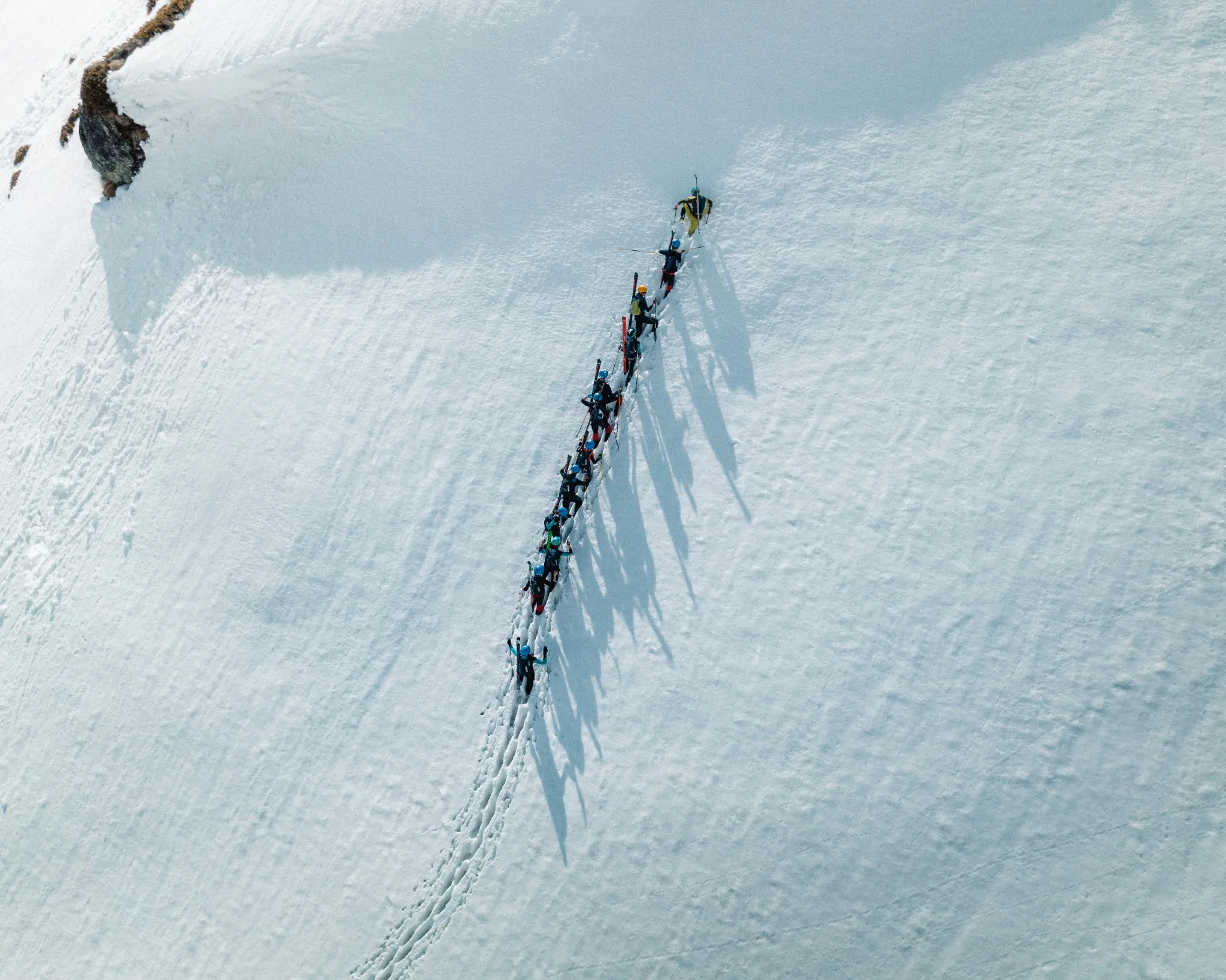 Groupe d’alpinistes en file indienne progressant sur une pente enneigée, vu du ciel.