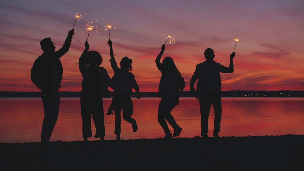 Silhouettes of people celebrating with sparklers at sunset.