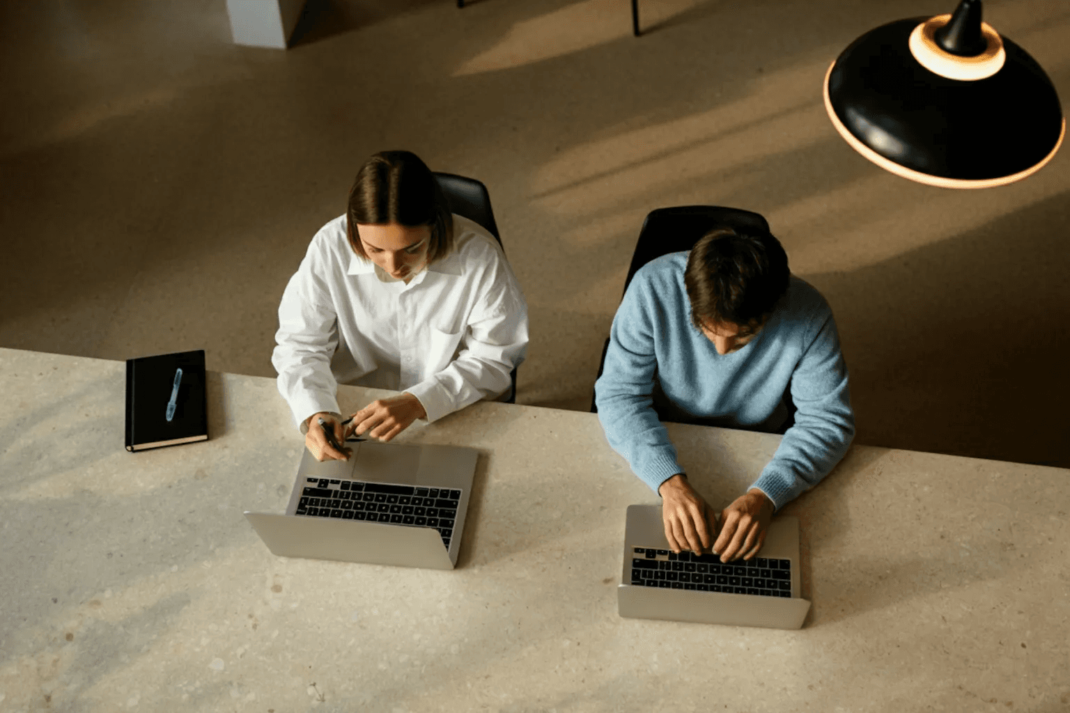 Man and woman working side by side at a desk, both focused on their laptops.