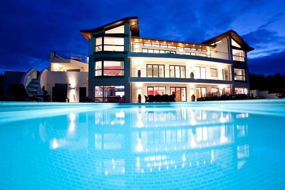 Modern luxury house with illuminated pool at twilight.