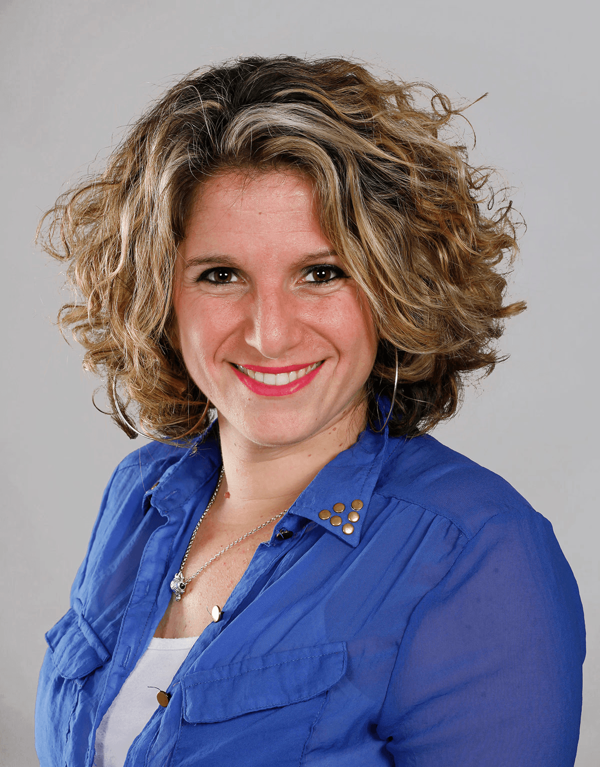 Minimal studio portrait of a confident woman in a white shirt, arms crossed, on a soft gray background.