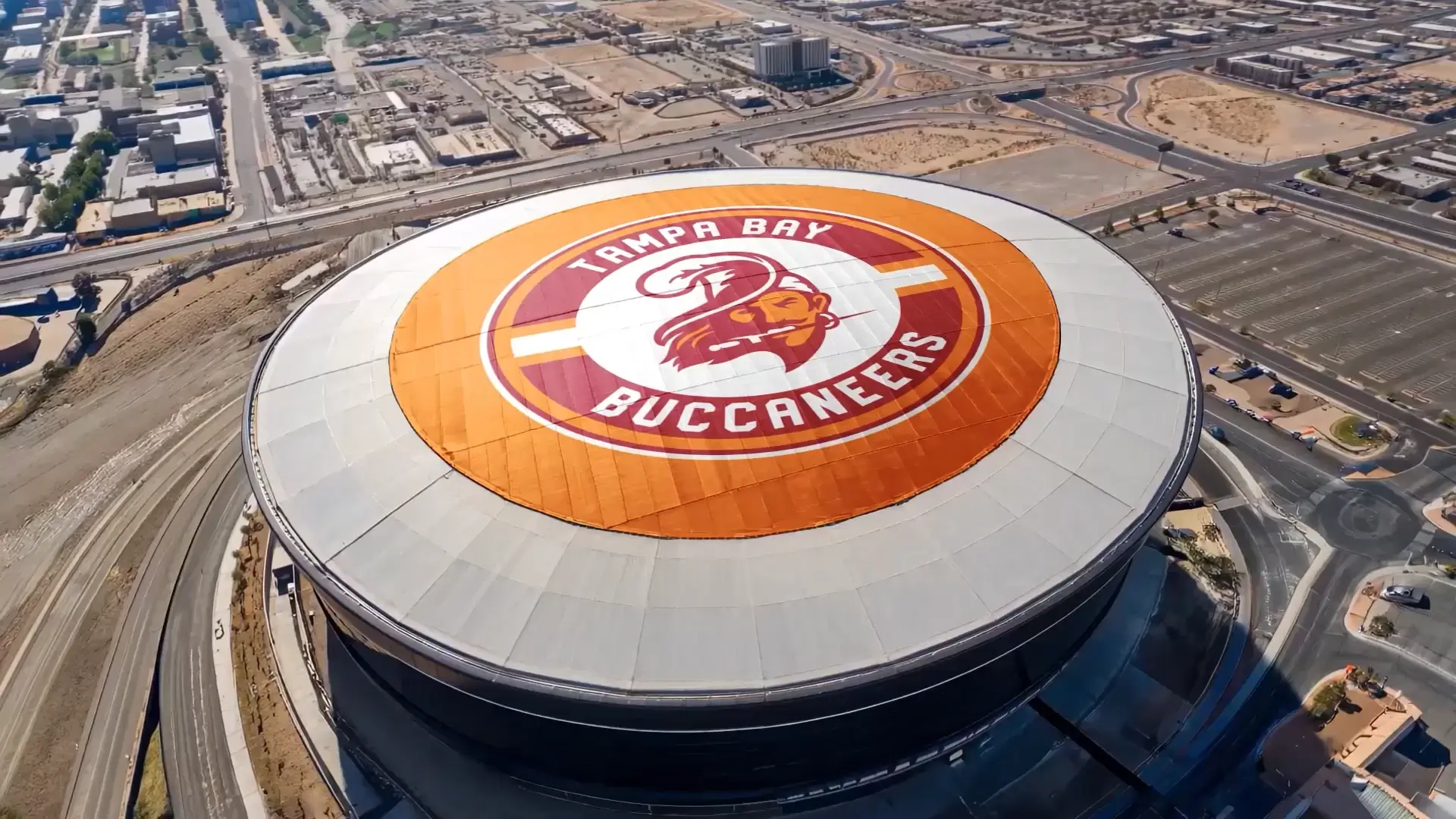 Aerial view of a domed stadium roof painted with the Tampa Bay Buccaneers logo and wordmark.