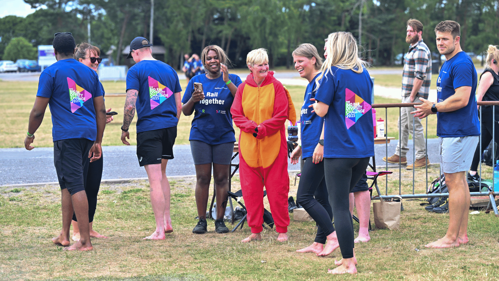 Outdoor team-building event with participants wearing matching blue shirts, taking part in inflatable obstacle courses and games, smiling and cheering, with the words 'ENTER A TEAM' in large bold white and green text across the image.