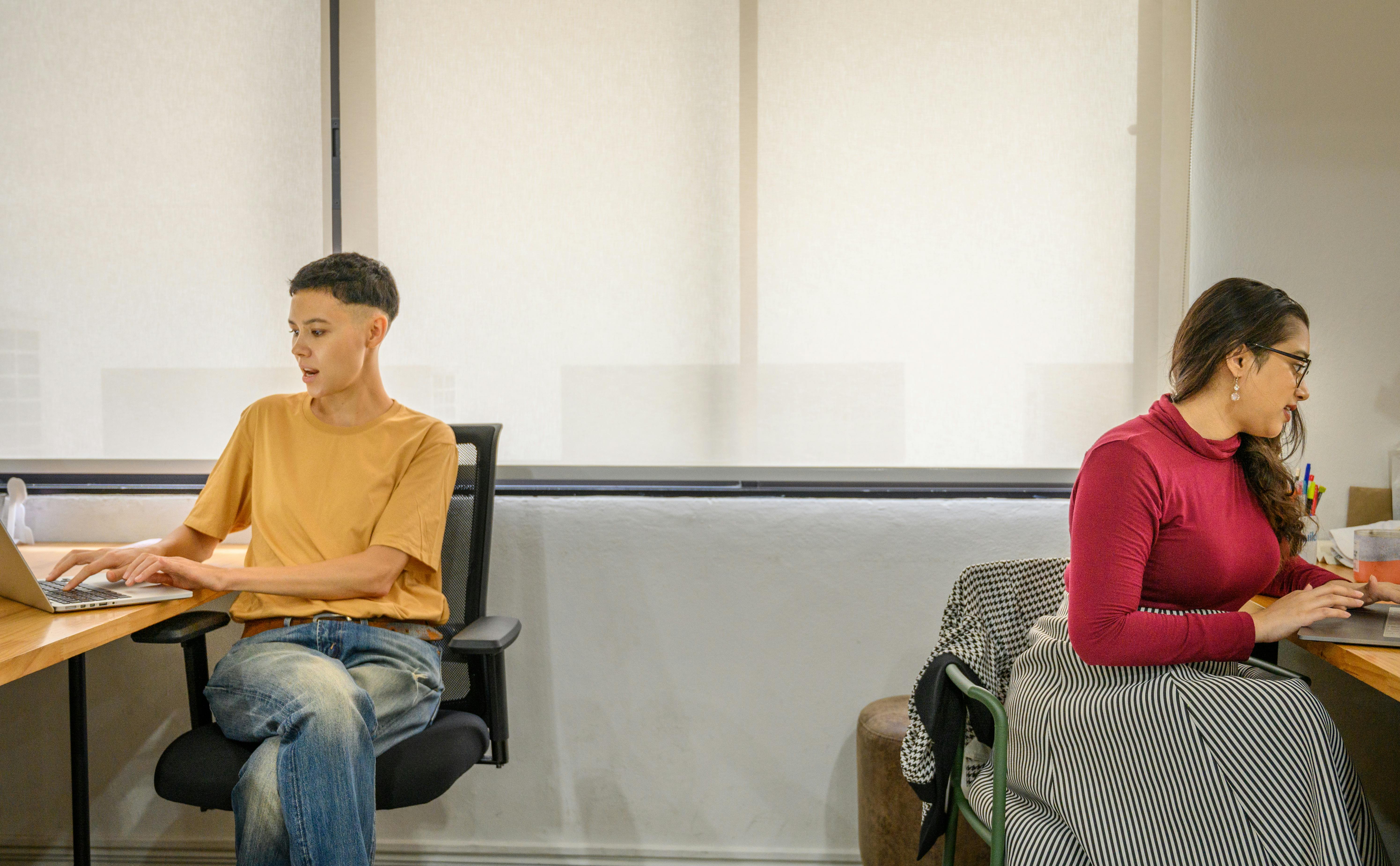 Due giovani al lavoro in ufficio su postazioni separate, fase di transizione post laurea tra primi impieghi e ripensamento del proprio percorso professionale