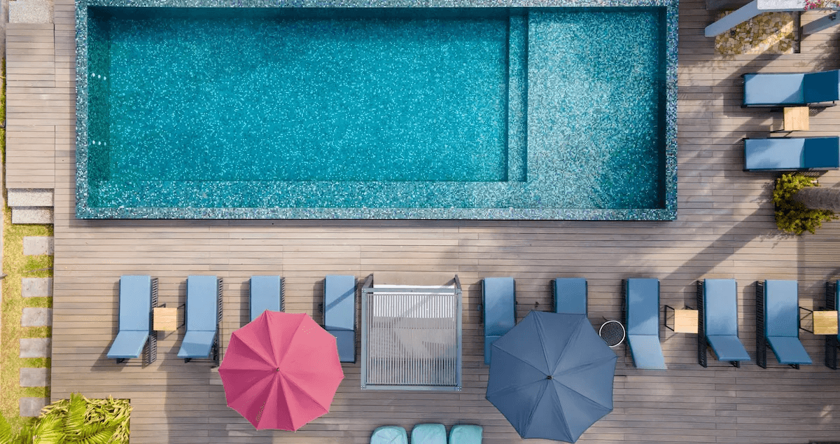 Aerial view of a modern rectangular swimming pool with surrounding timber deck, sun loungers, and colourful umbrellas.