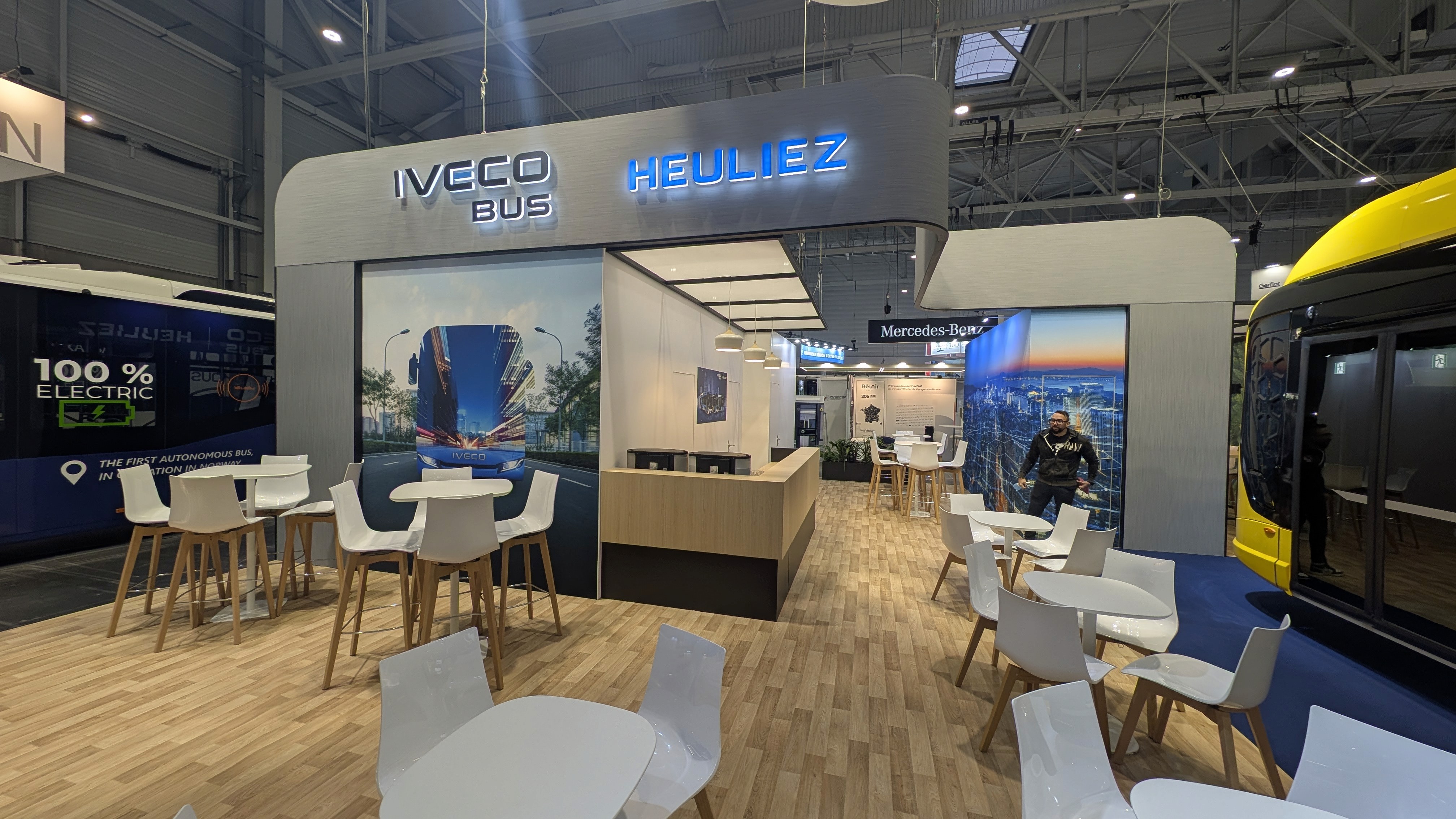 Stand IVECO Bus Heuliez RNTP 2025 par Expace – vue d'ensemble du stand avec zone lounge bois, écrans LED et présentation gamme véhicules transport en commun