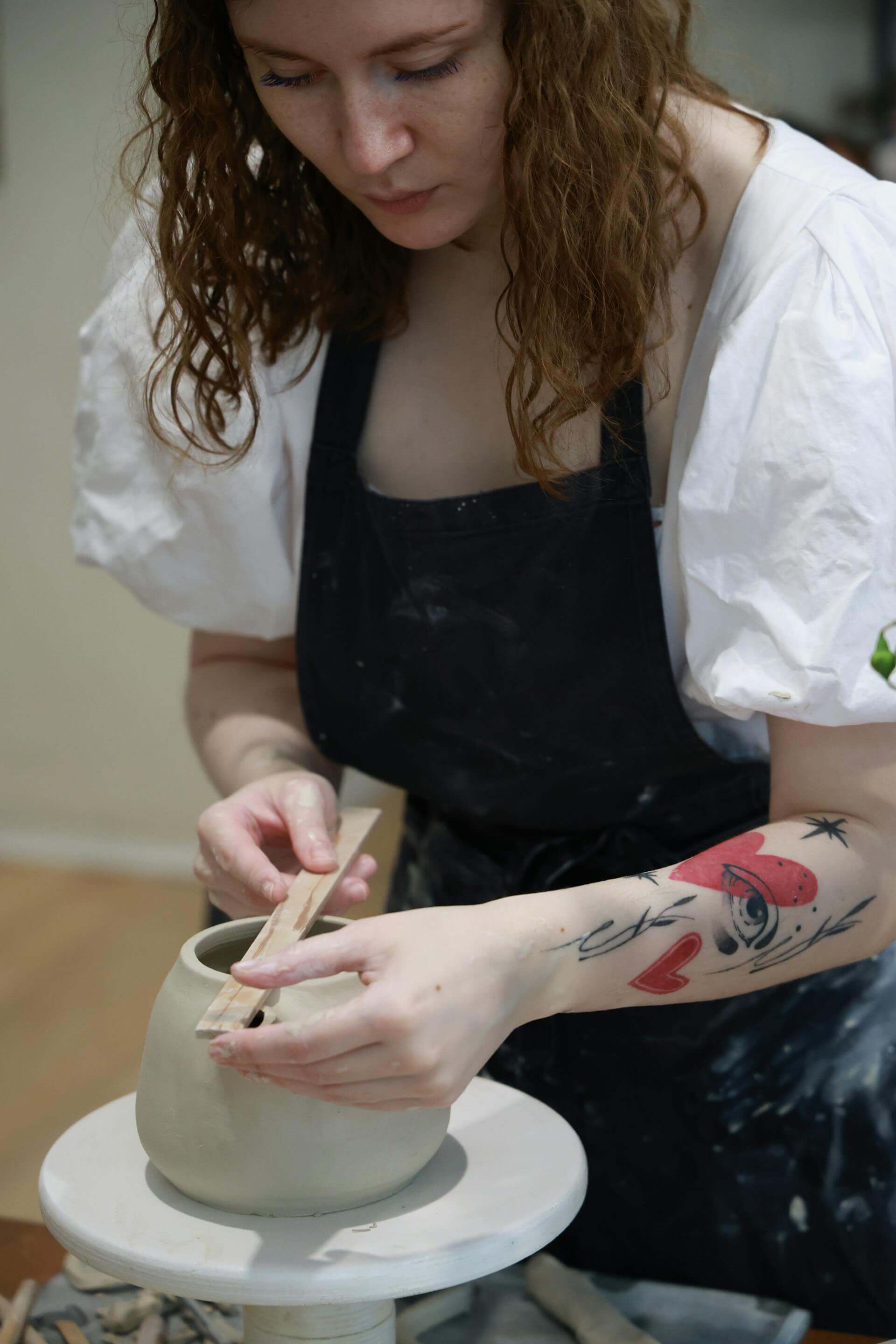 A woman skillfully shapes a clay pot on a table, showcasing her craftsmanship and focus in the art of pottery