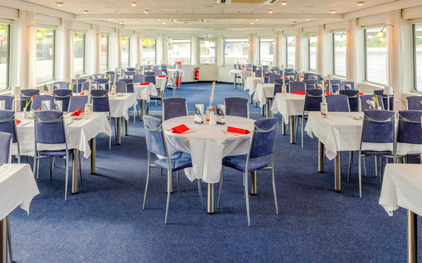 Area makan dengan meja yang sudah tertata dan kursi biru di kapal pesiar MS Vienna.