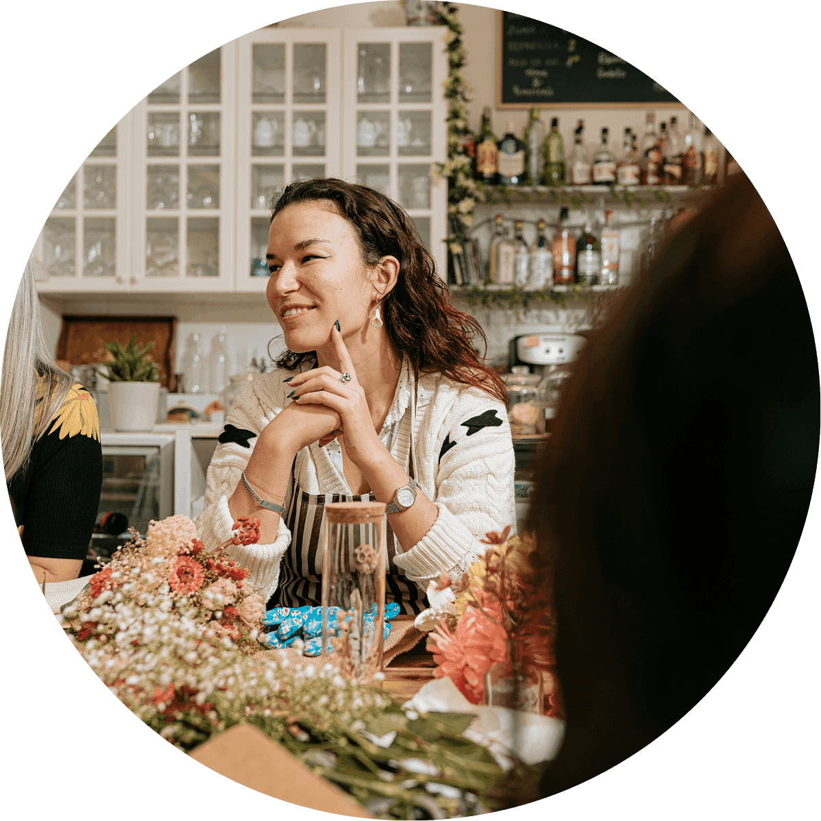 Woman sits at a table in a cozy restaurant setting holding a drink and smiling during a conversation